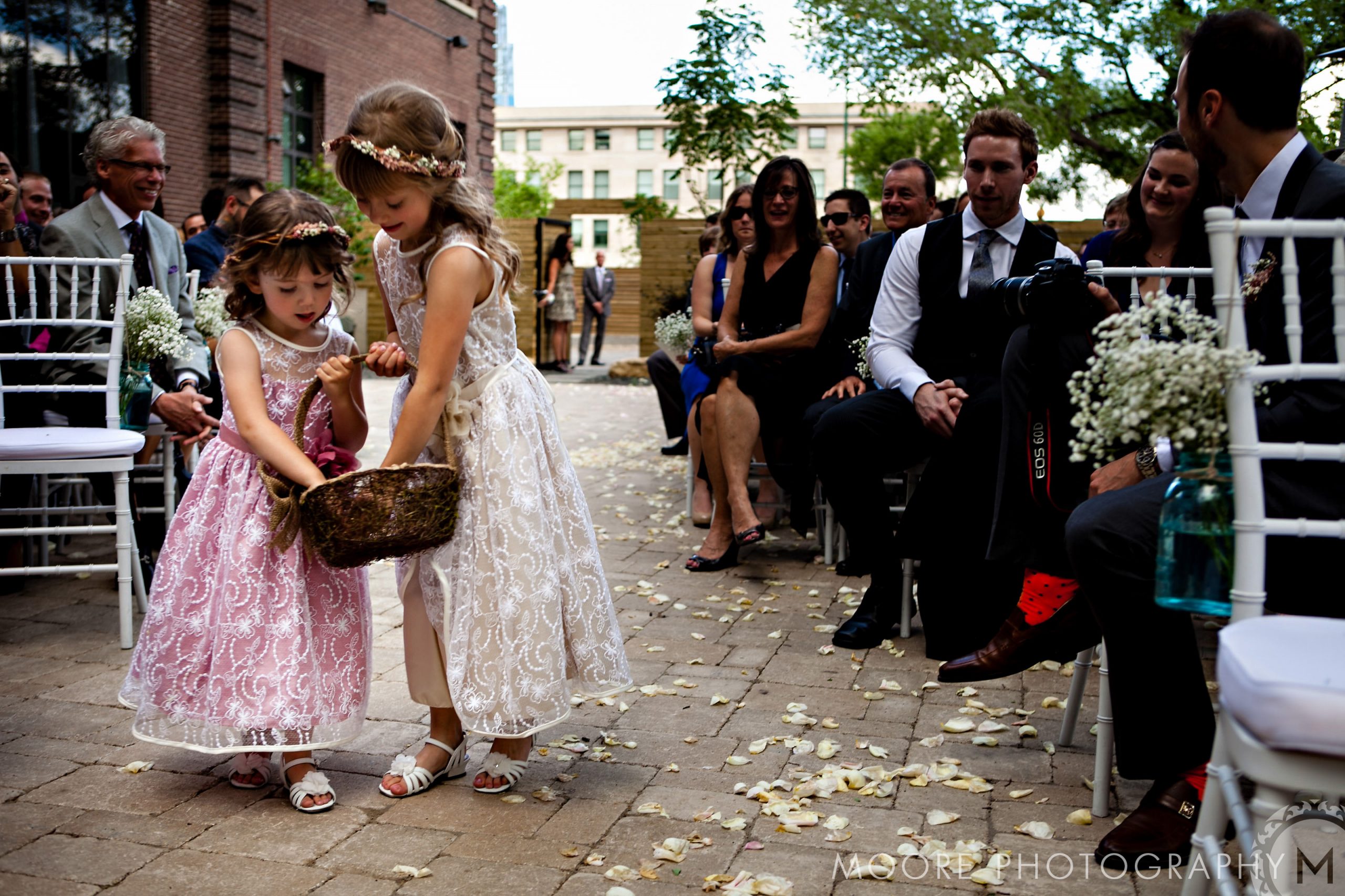 Two young flower girls scatter petals down the aisle at a Winnipeg wedding venue.