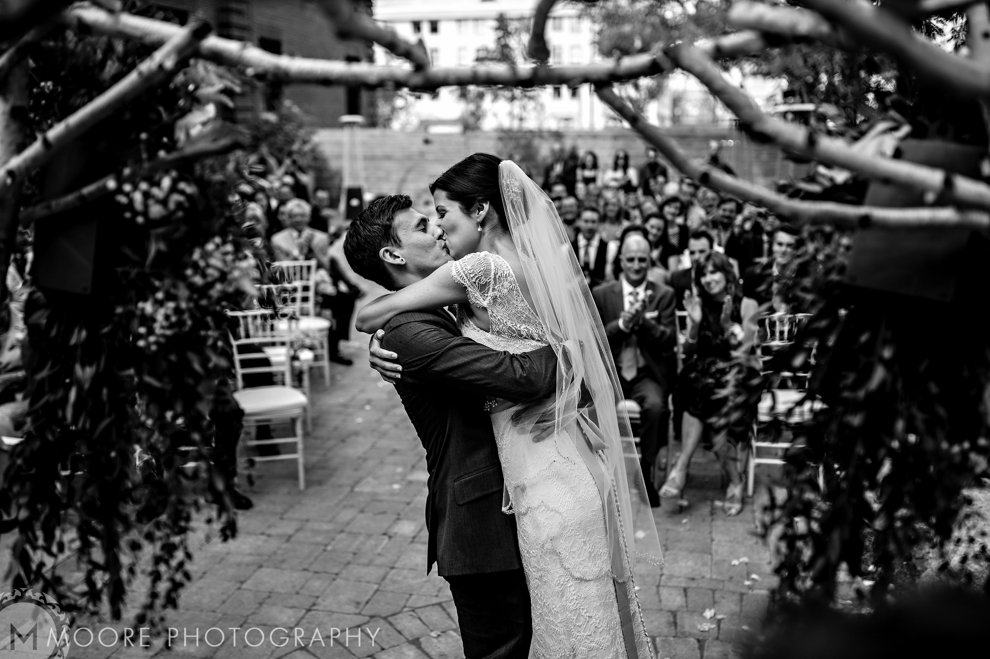 Bride and groom kiss at an outdoor Winnipeg wedding venue as guests watch.