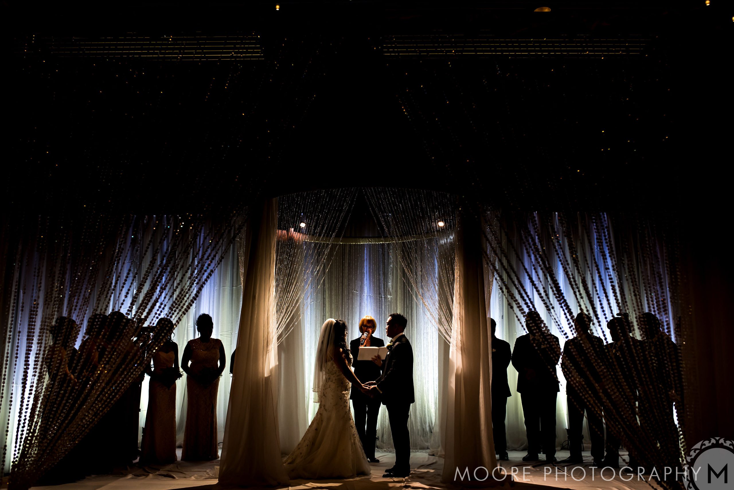 Bride and groom at altar, silhouetted with wedding party, in Winnipeg wedding venue's dramatic lighting.