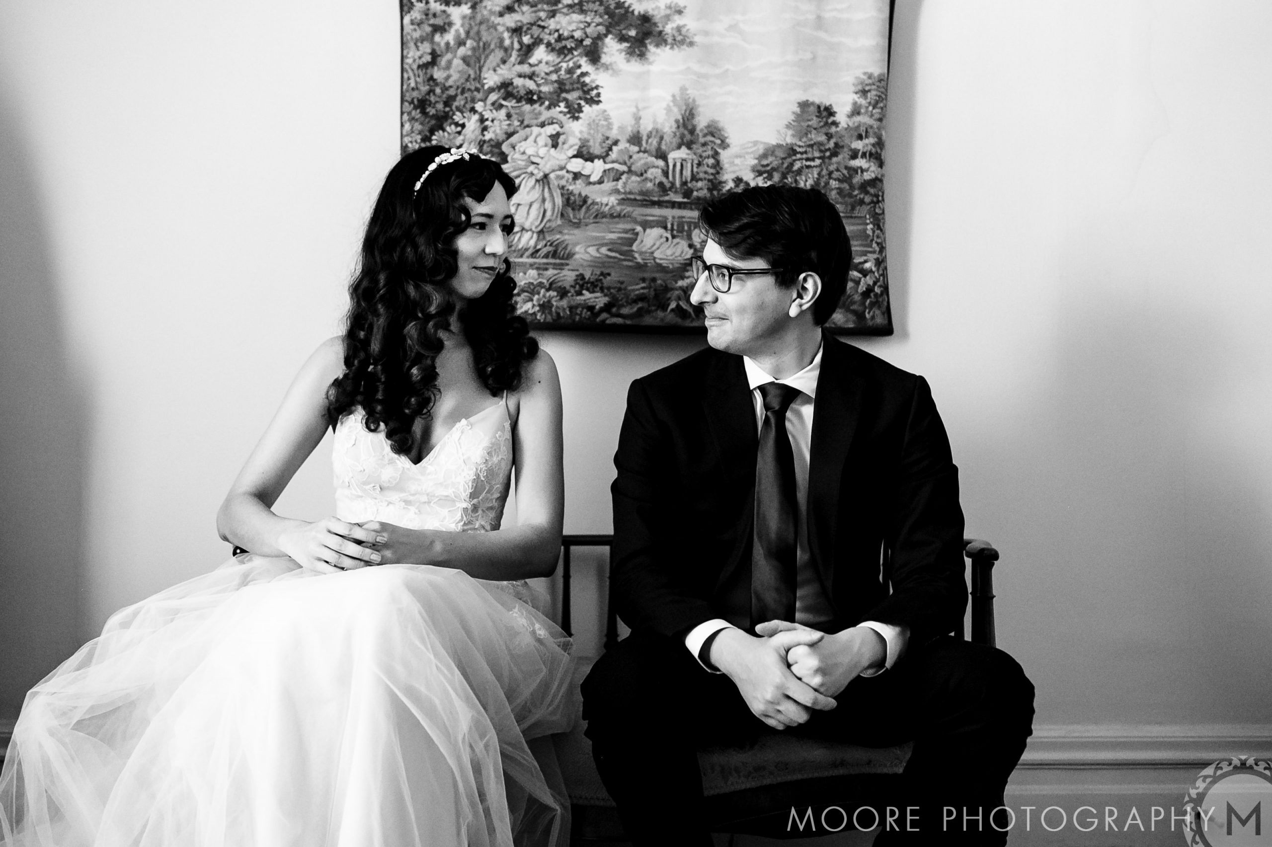 Bride in gown and groom in suit smiling at each other, Winnipeg wedding venue, black and white.