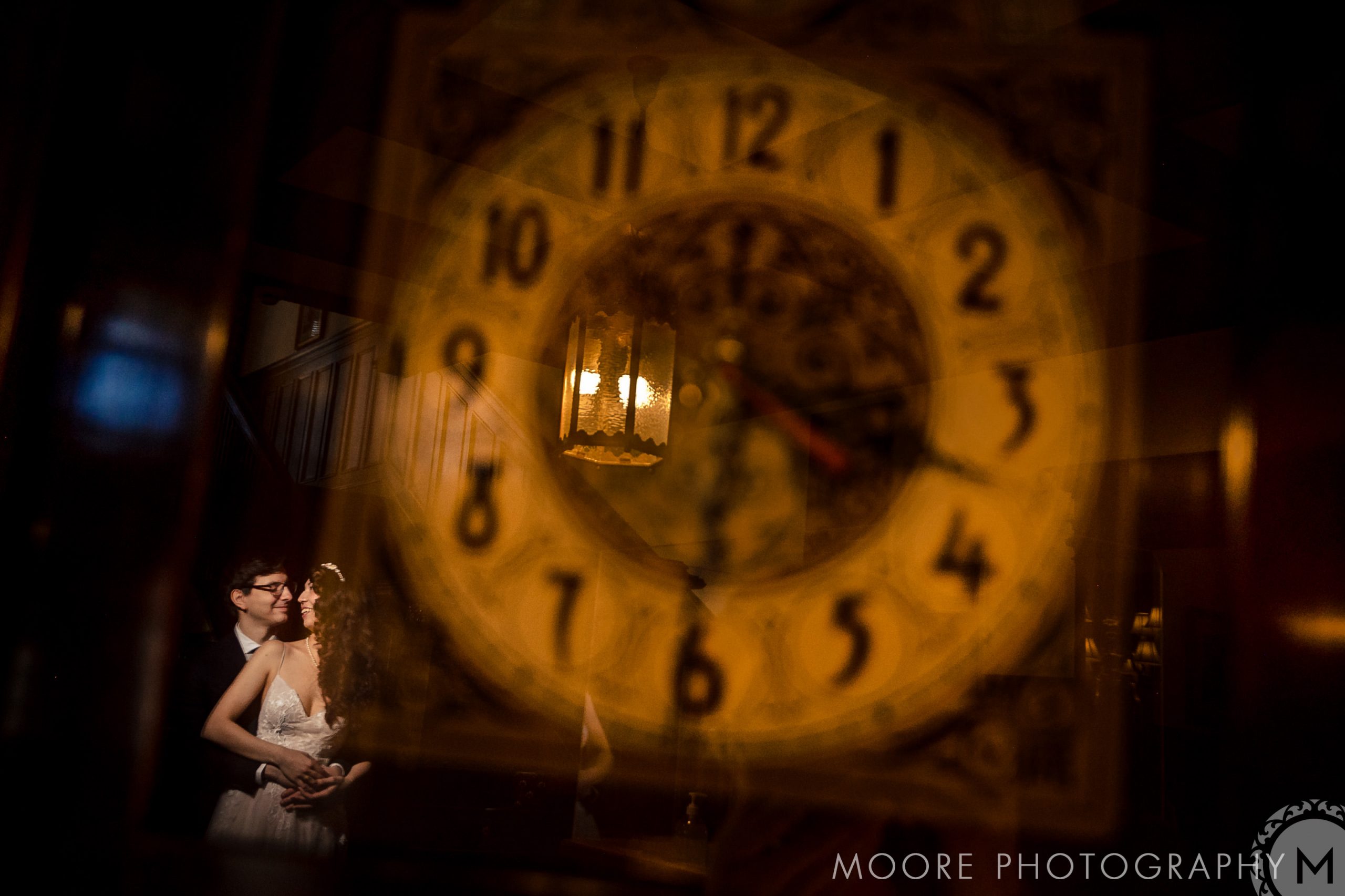 A couple embraces behind a large, blurred clock face at Winnipeg wedding venues.
