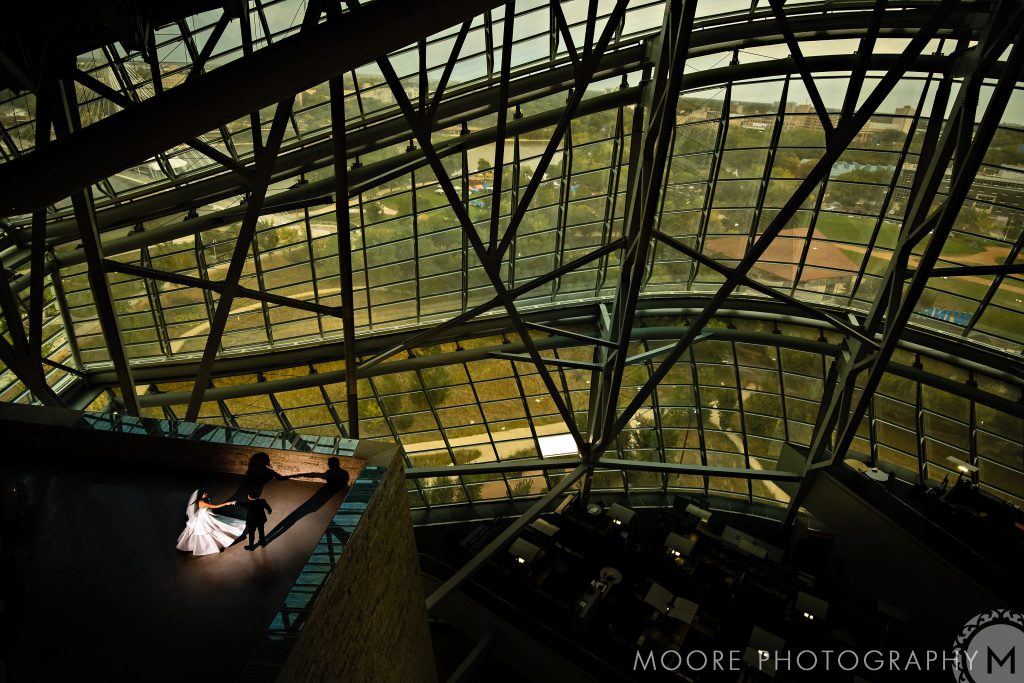 Bride and groom dance under Winnipeg wedding venues' glass architecture, with a scenic view.