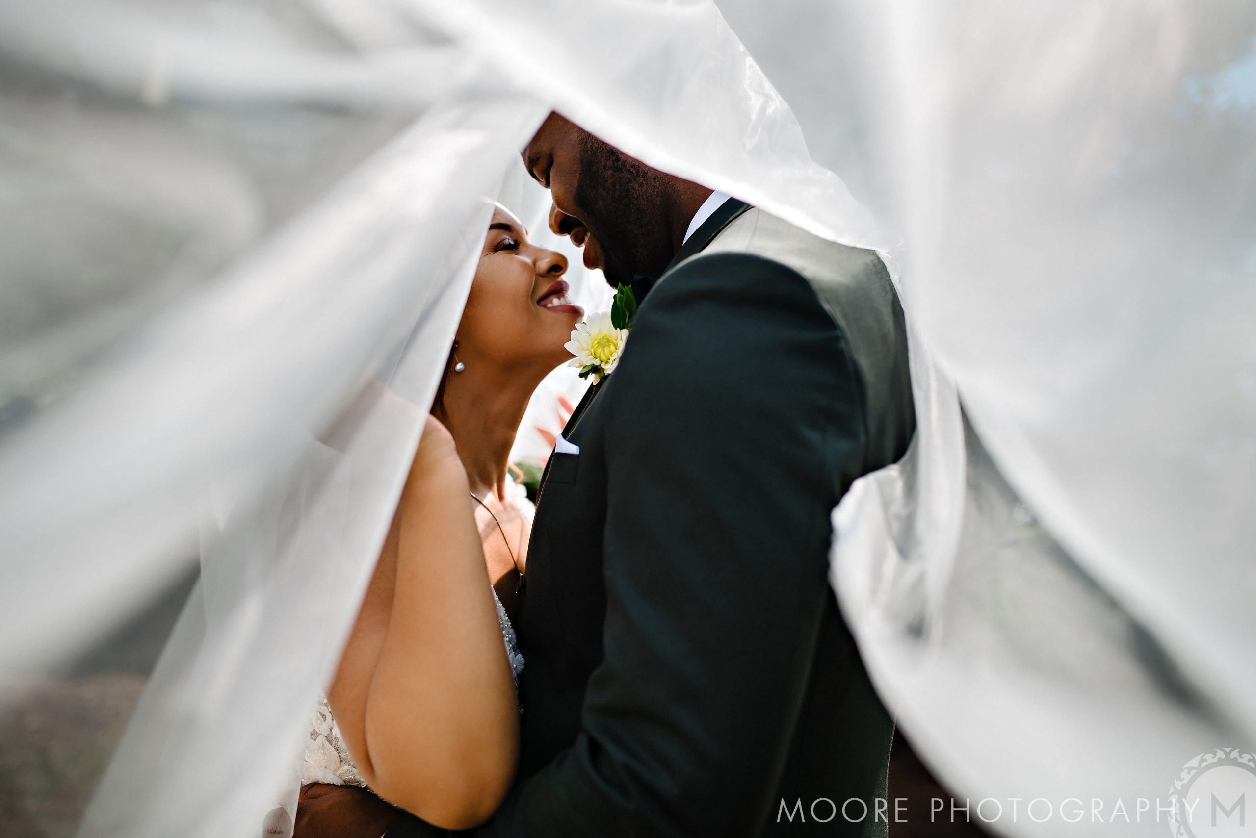 Bride and groom at Winnipeg venue embrace under a flowing white veil, sharing a joyful moment.