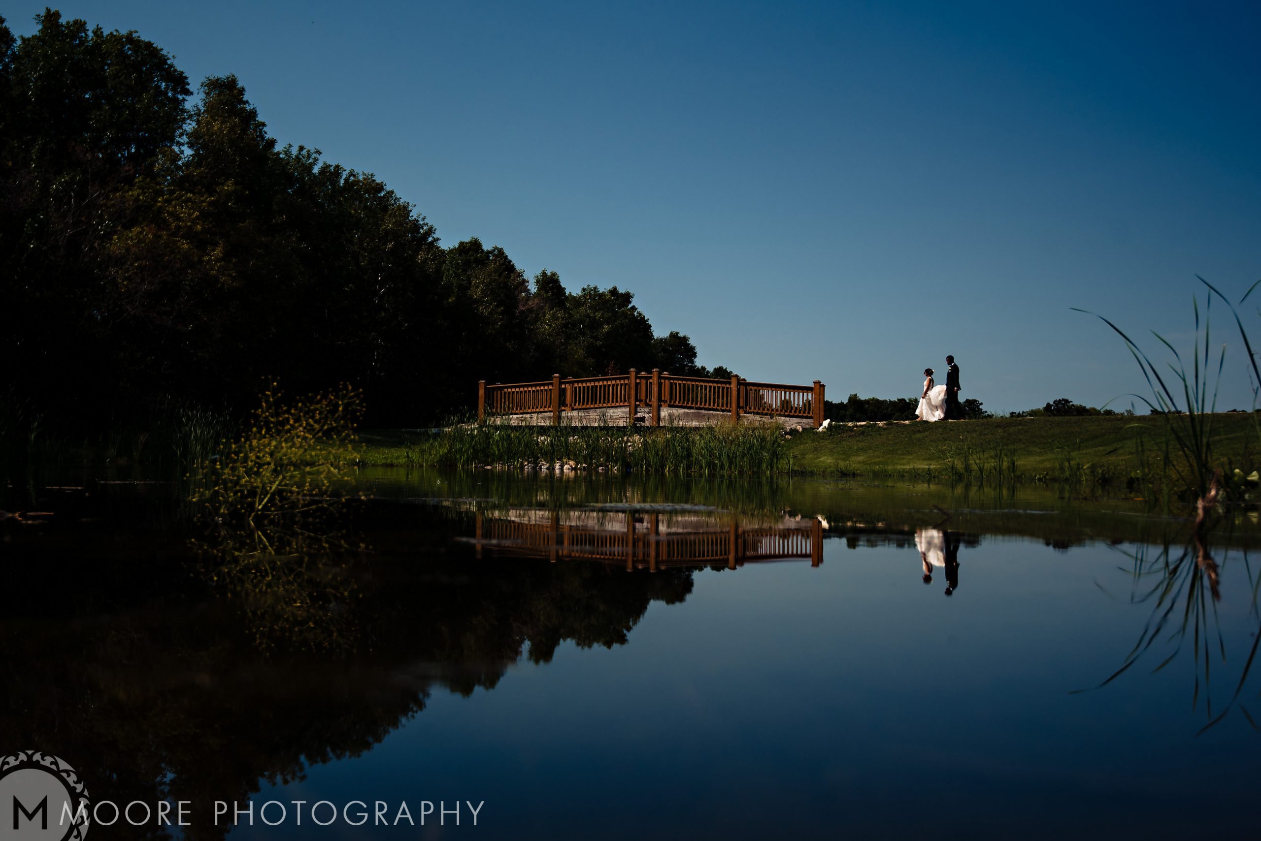 bride and groom walking across a bridge at whitetail meadows in manitoba