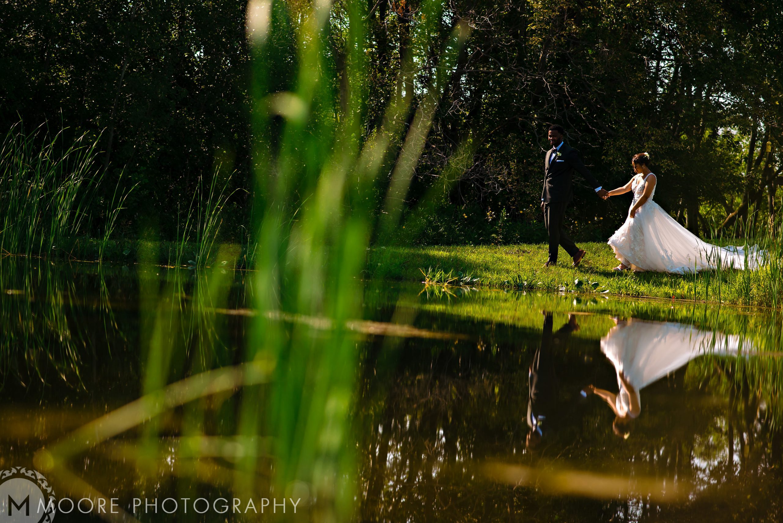 Bride and groom at a Winnipeg wedding venue, their reflection shimmering in the pond.