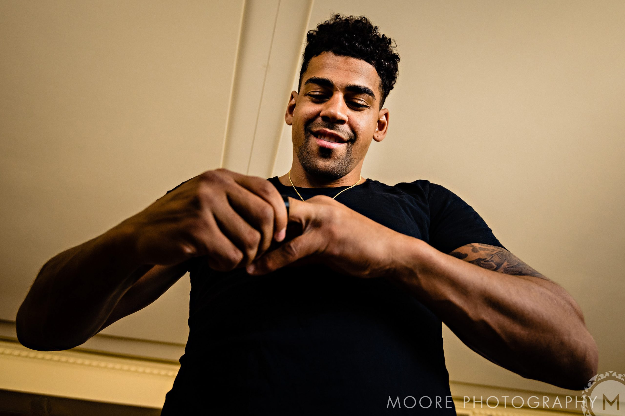 Andrew Harris in a black shirt, looking down while holding an object indoors.