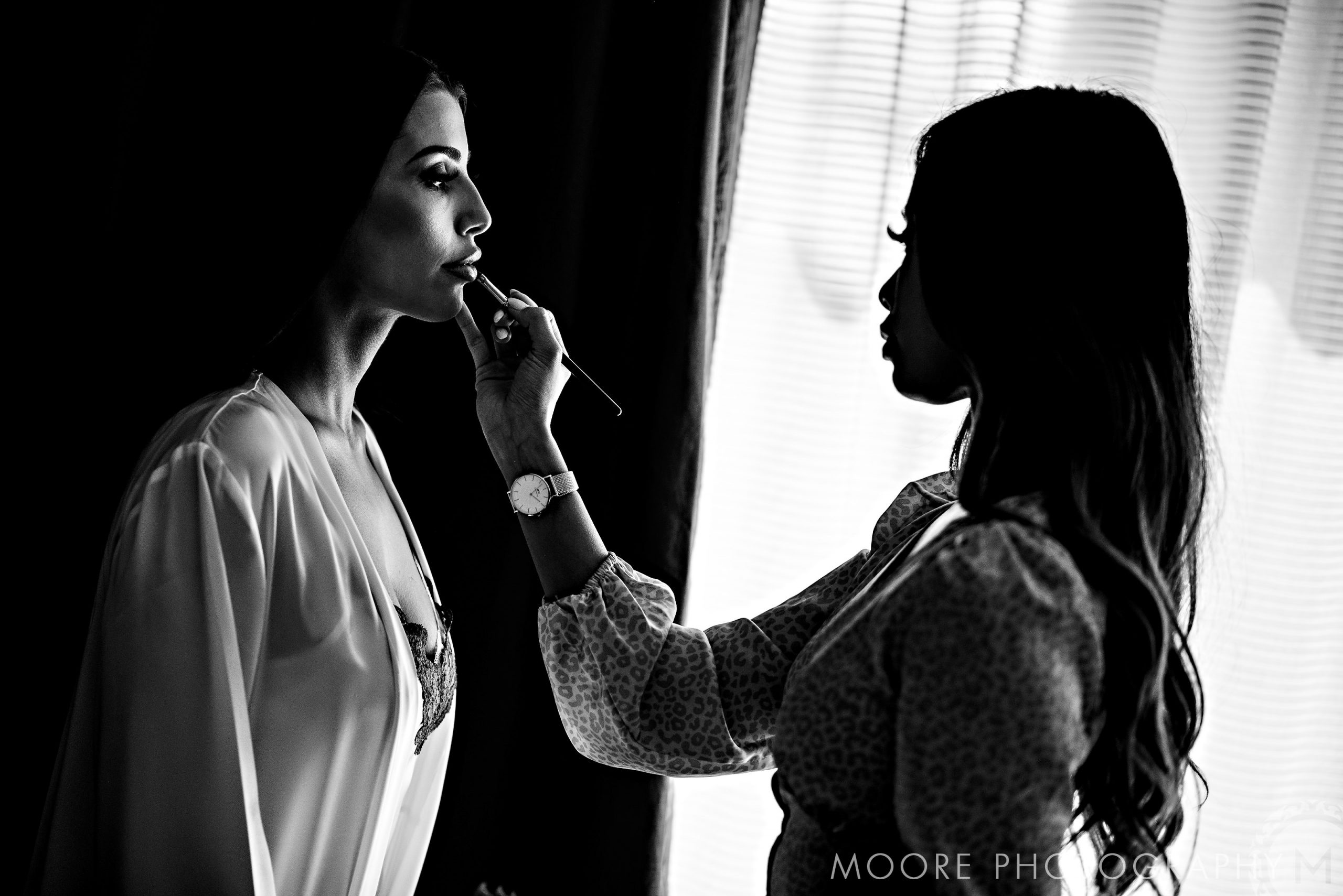 Andrew Harris, a silhouetted makeup artist, applies lipstick by window light.