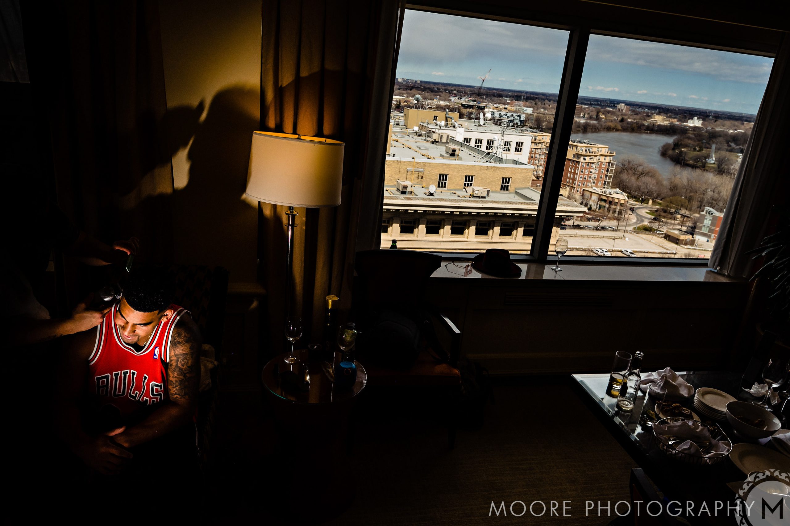 Andrew Harris in a jersey getting styled in a hotel room with city view.