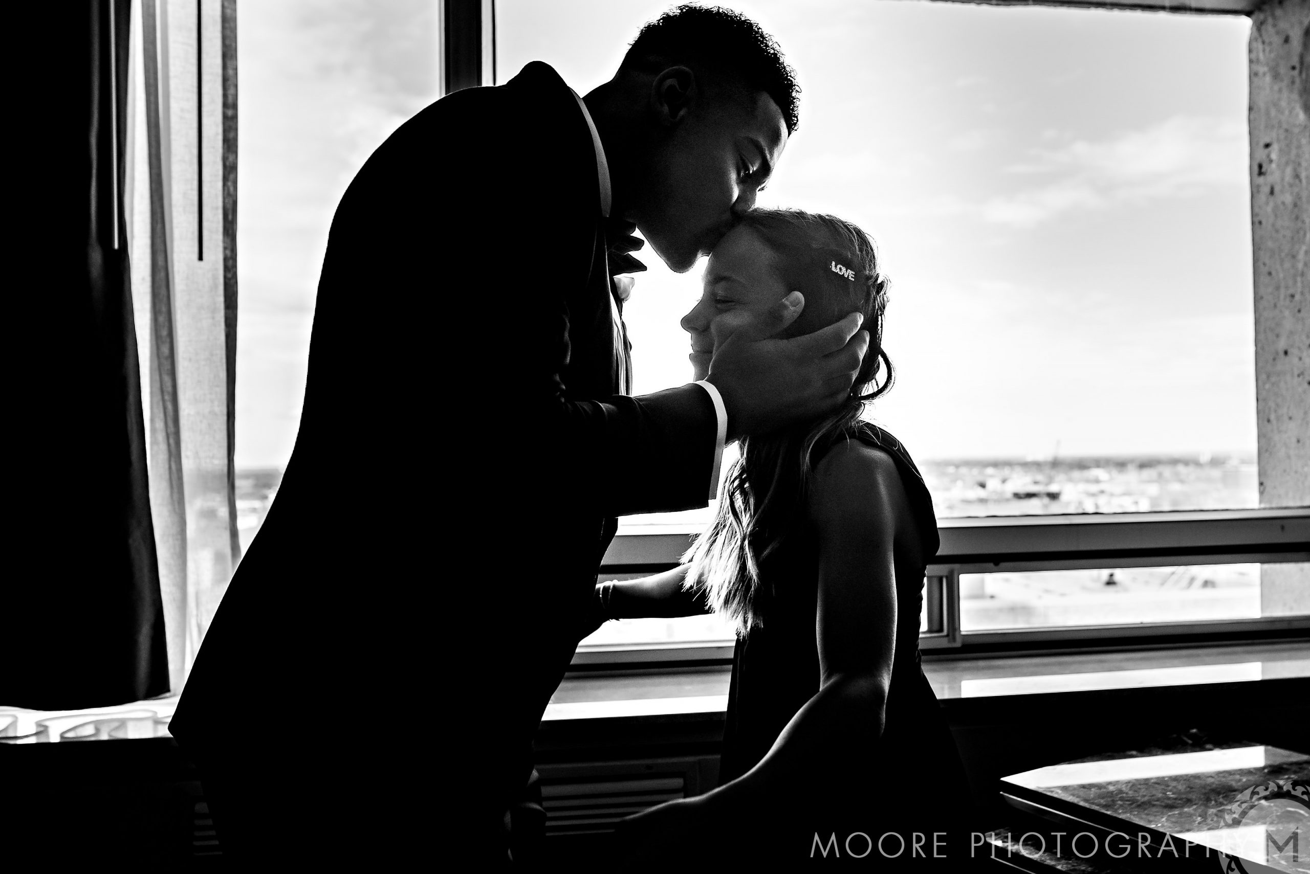 A man kisses a girl's forehead in the sunlight at Andrew Harris's wedding.