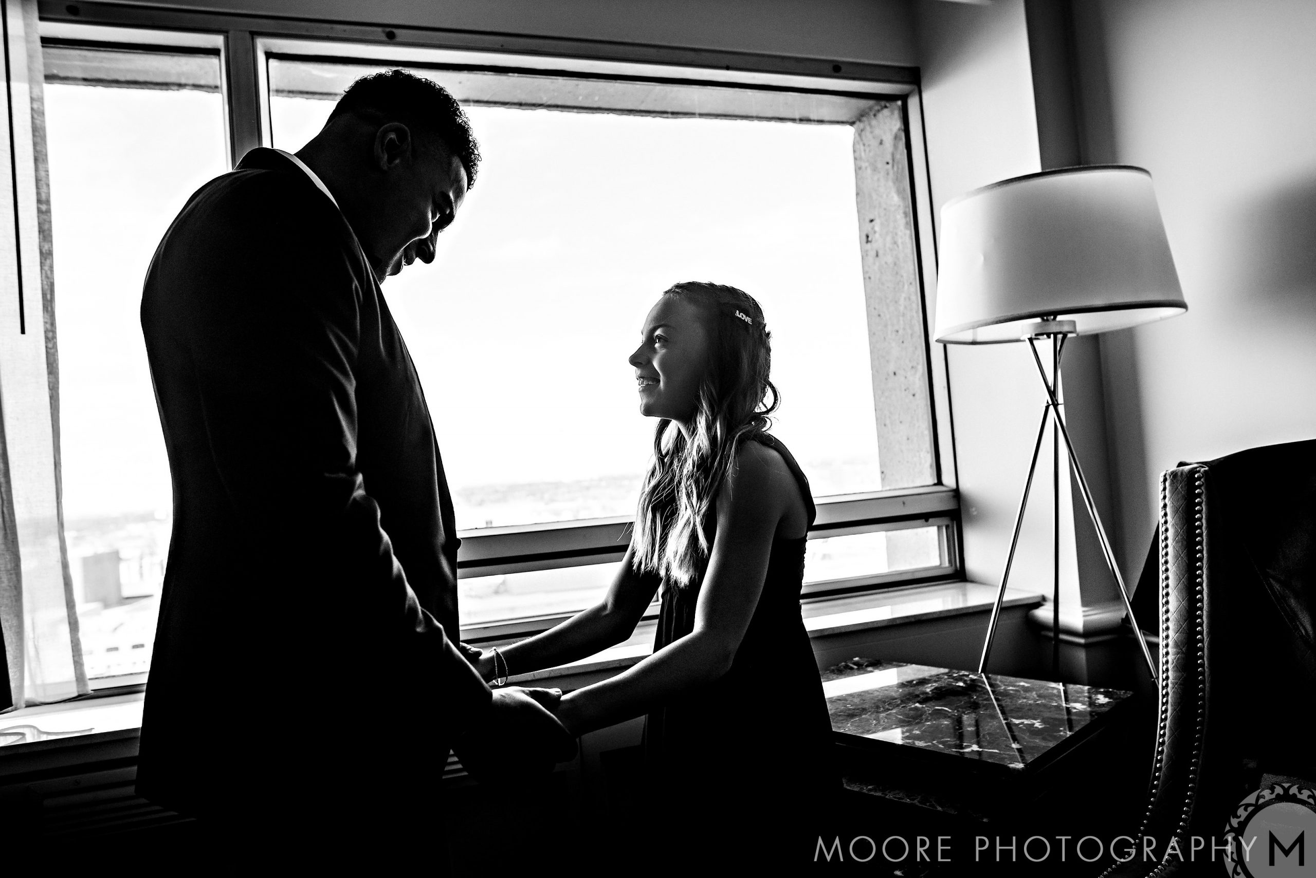 Couple holding hands and smiling in window-lit room at Andrew Harris wedding.