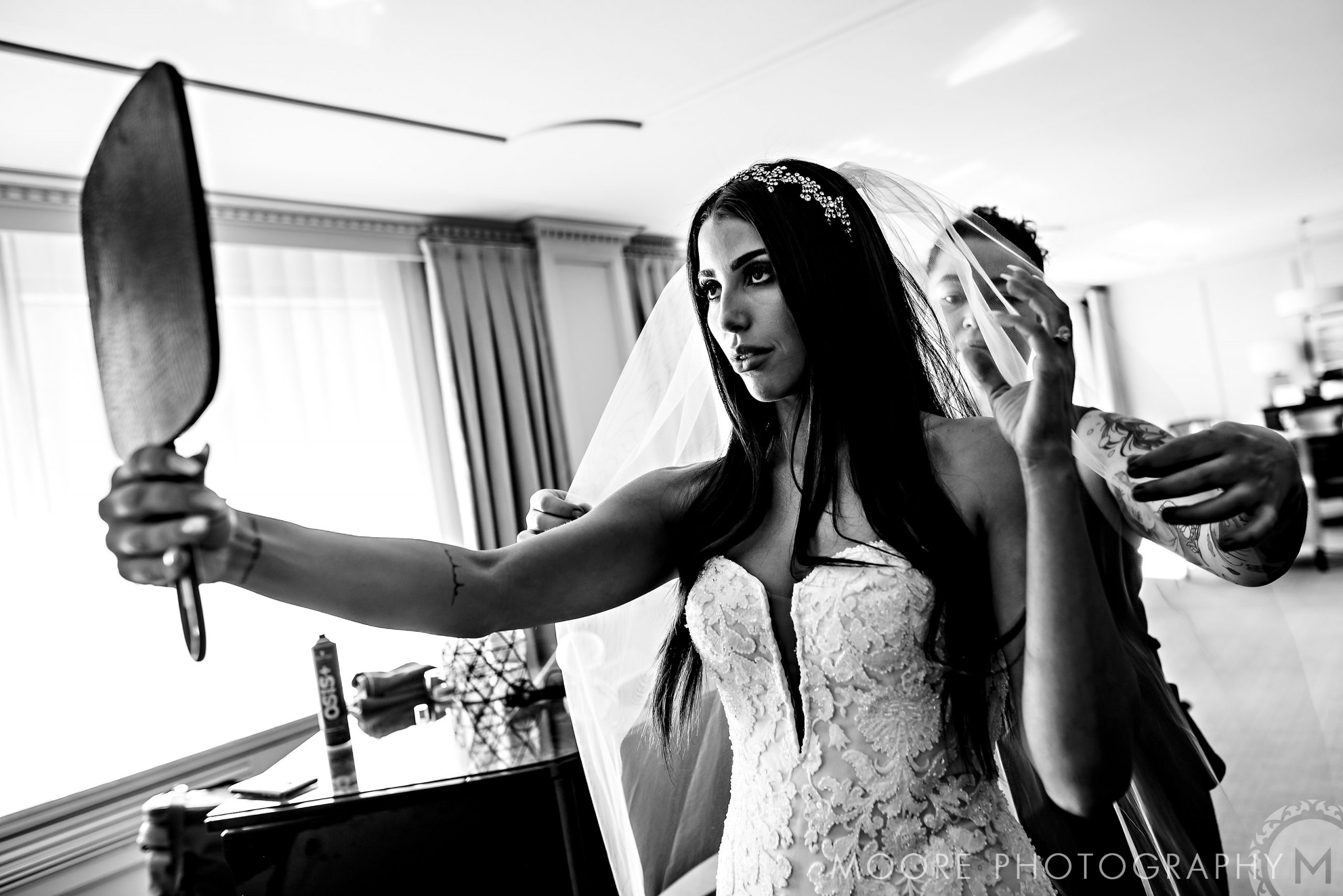 Bride adjusting her veil, captured gracefully by Andrew Harris, in a bright room.