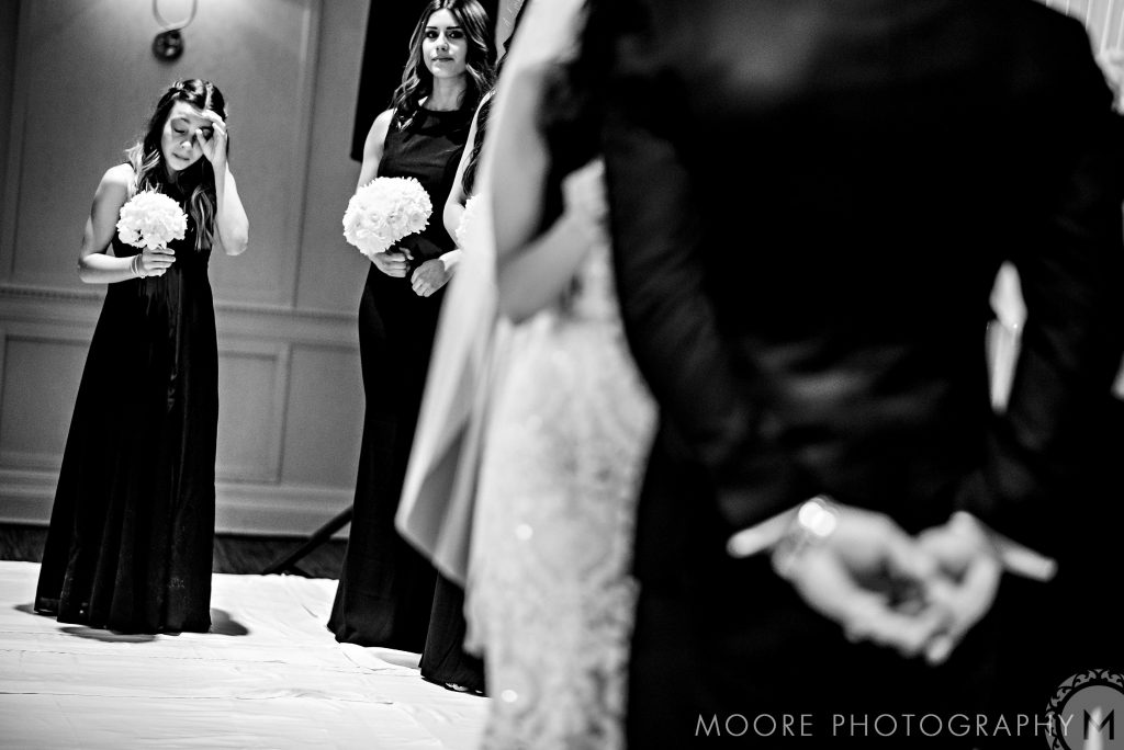 Bridesmaids with bouquets stand by Andrew Harris at a dimly lit wedding ceremony.