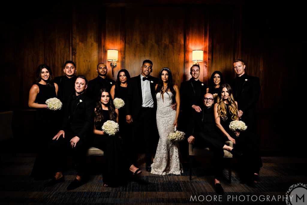 Andrew Harris wedding party in formal attire poses against dark wood background indoors.