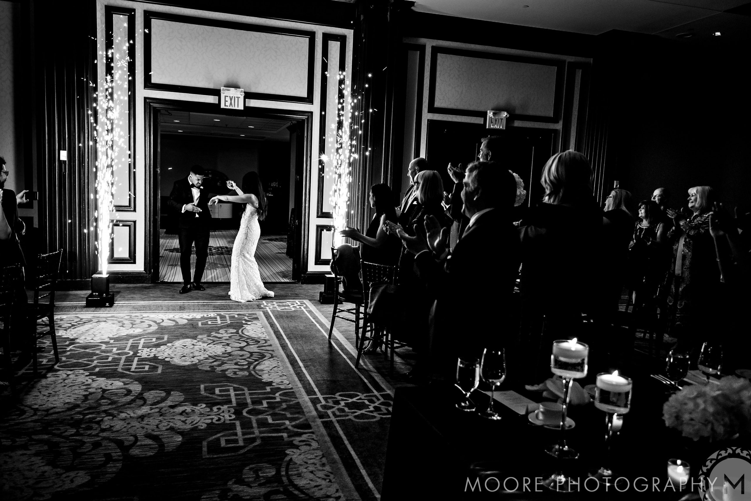 Andrew Harris and his bride enter a dimly lit room, greeted by applauding guests.
