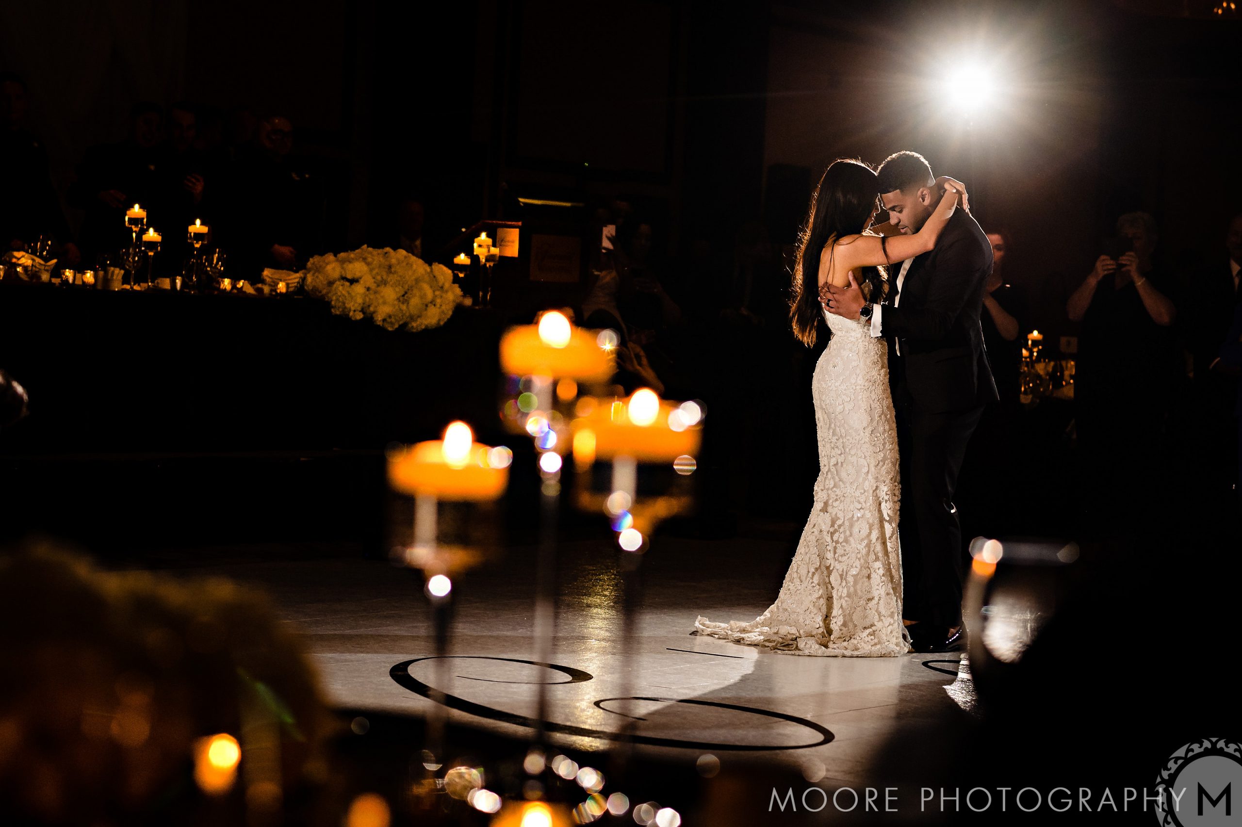 A couple dances in a dimly lit ballroom at a Winnipeg wedding venue, surrounded by guests.