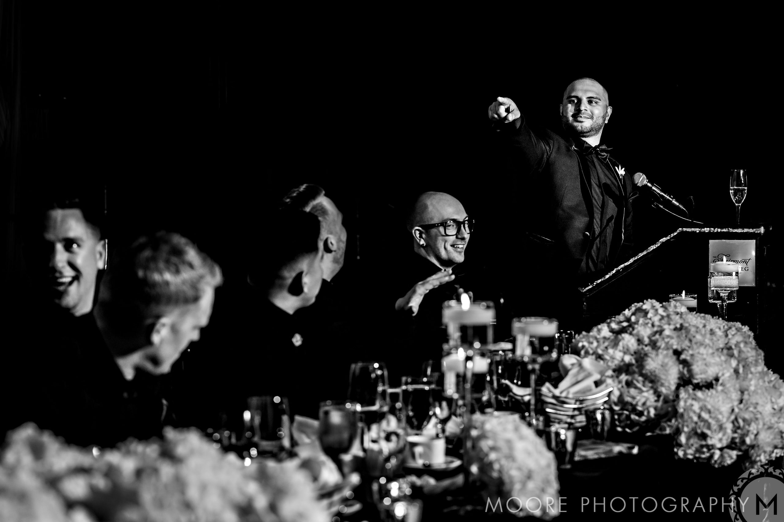Andrew Harris giving a speech at a formal event, guests seated and smiling, black and white photo.