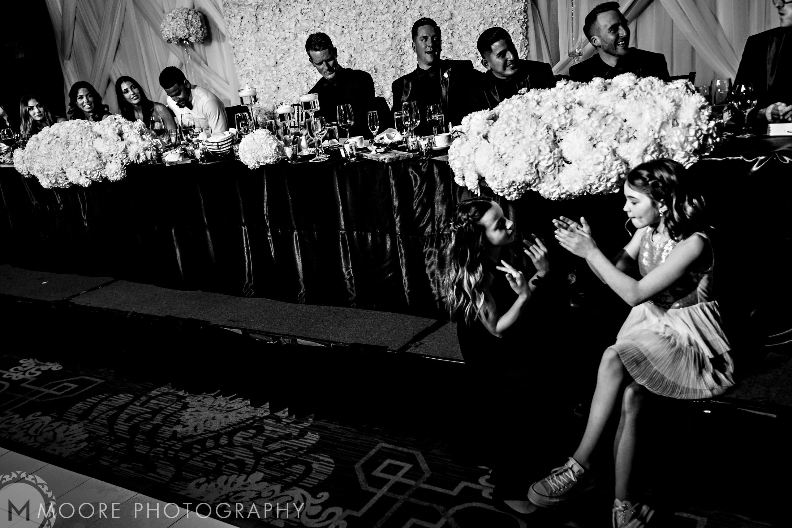 Two girls clapping near Andrew Harris's wedding head table, guests seated behind.
