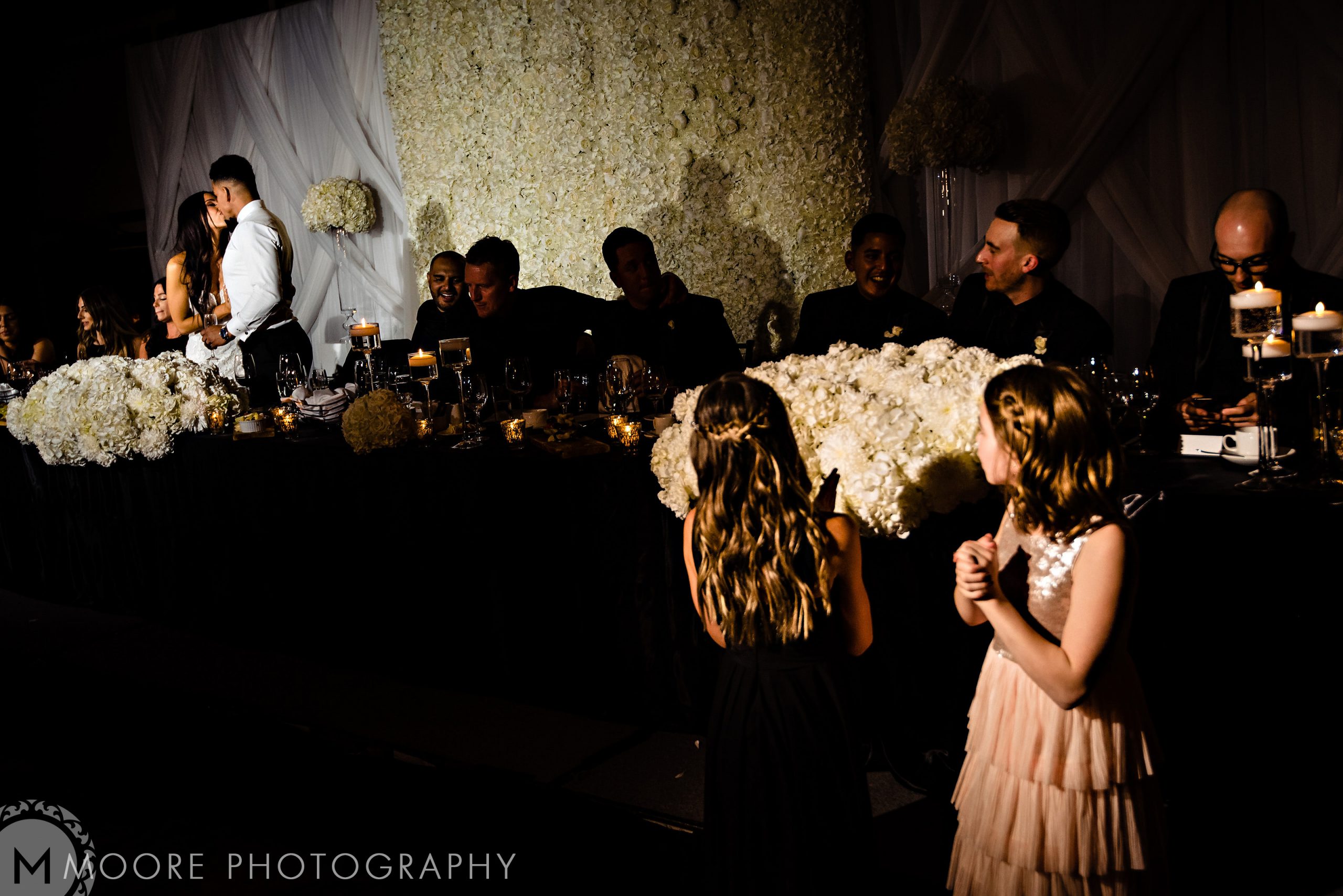 Andrew Harris wedding: couple hugging near a flower table; guests and girls in dresses nearby.