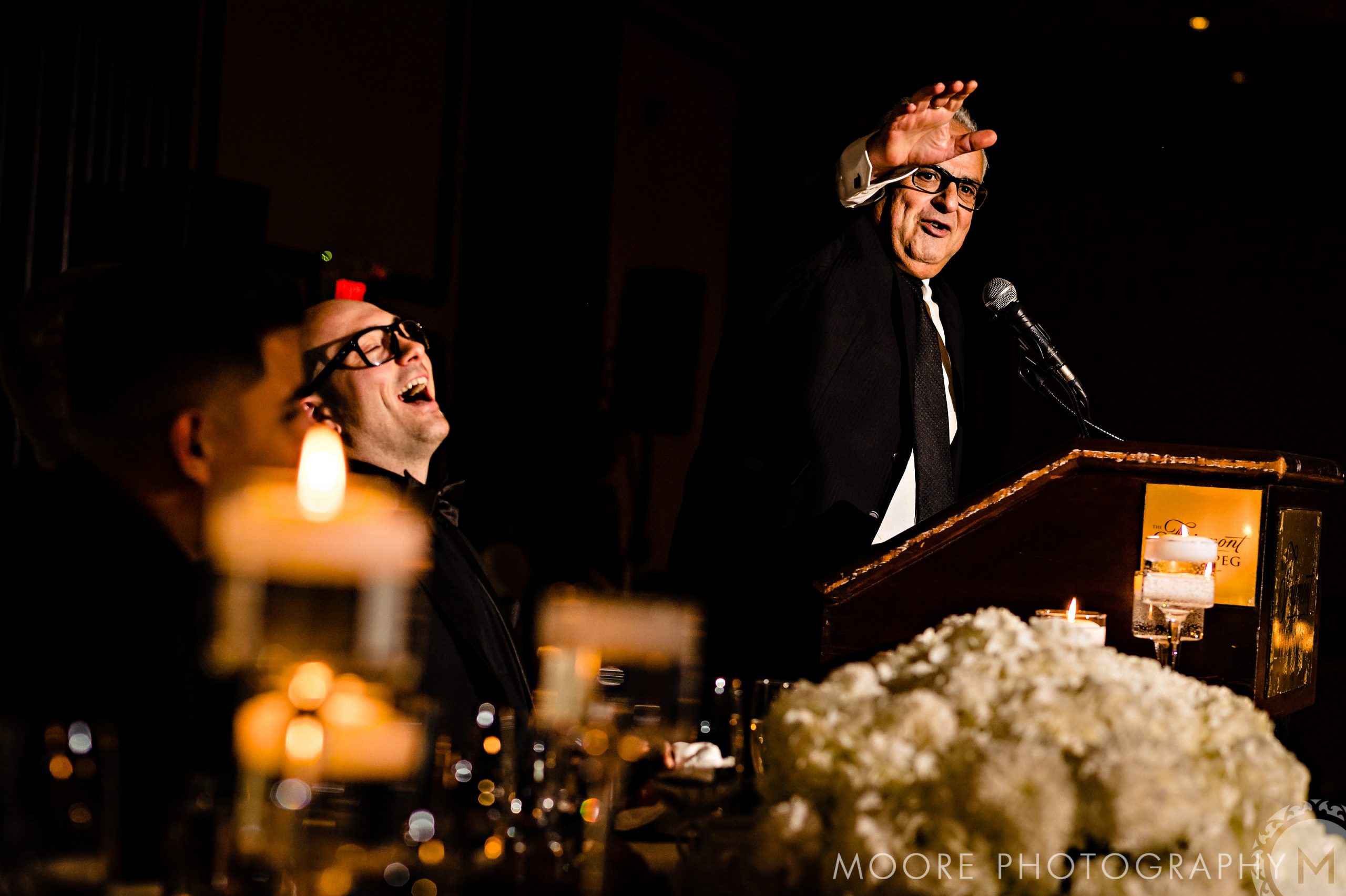 Andrew Harris laughing at a speech during his wedding with floral and candle decor.