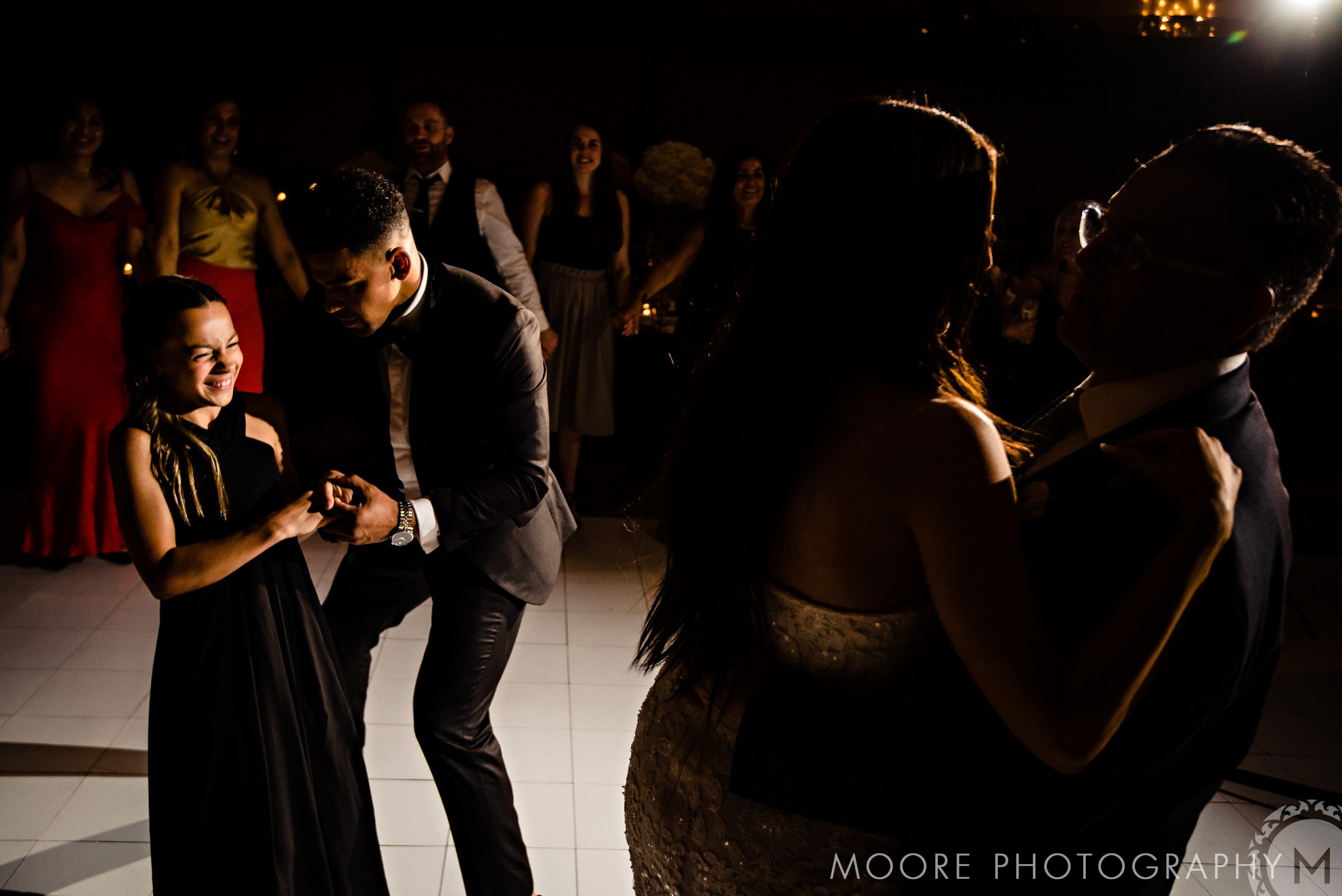 People dancing at Andrew Harris's lively wedding in formal attire under dim lighting.