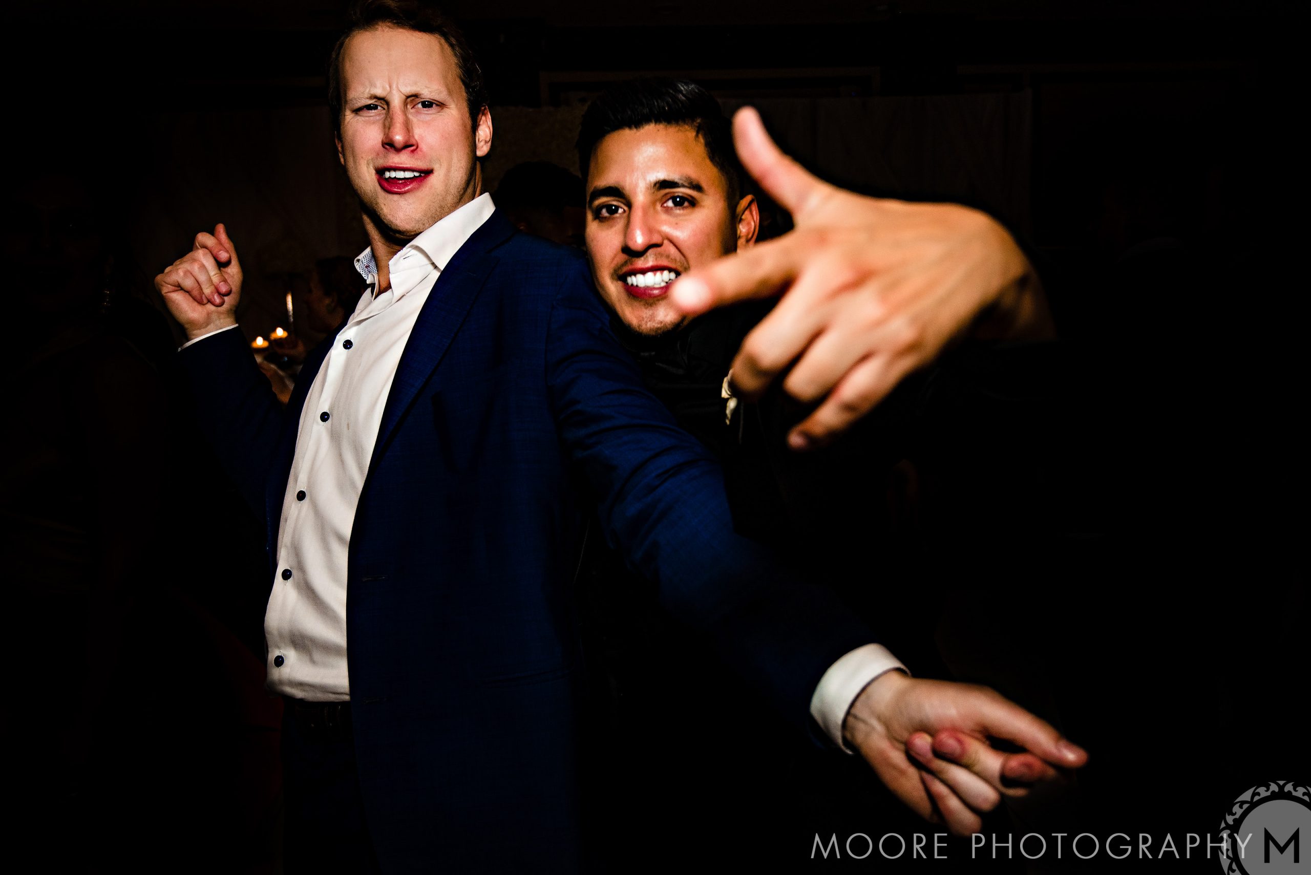 Andrew Harris and a friend pose energetically, one pointing to the camera in a dark setting.