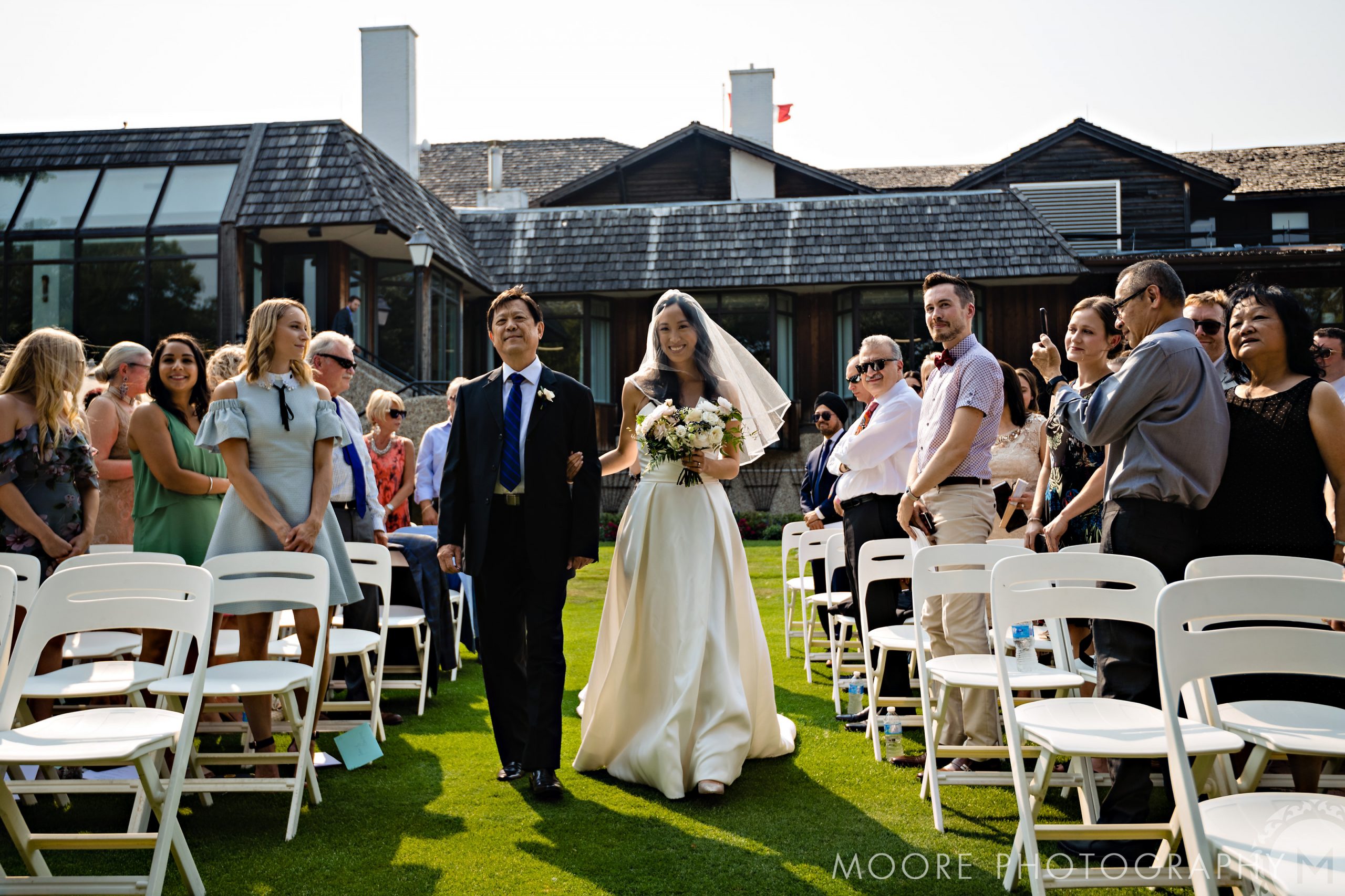 Bride walks down the aisle with a man at a picturesque Winnipeg wedding venue outdoors.