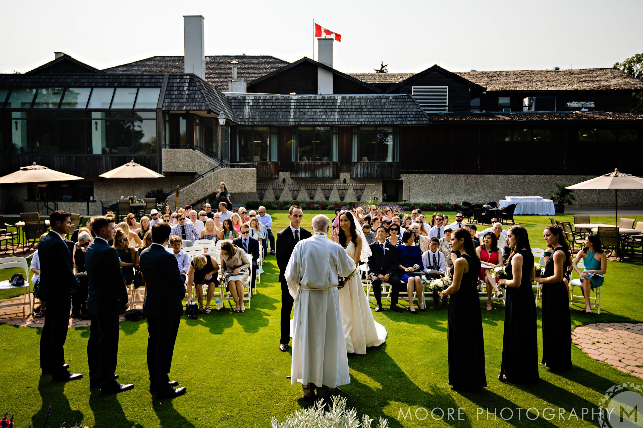 Outdoor wedding in Winnipeg with guests on a lawn before a grand building.