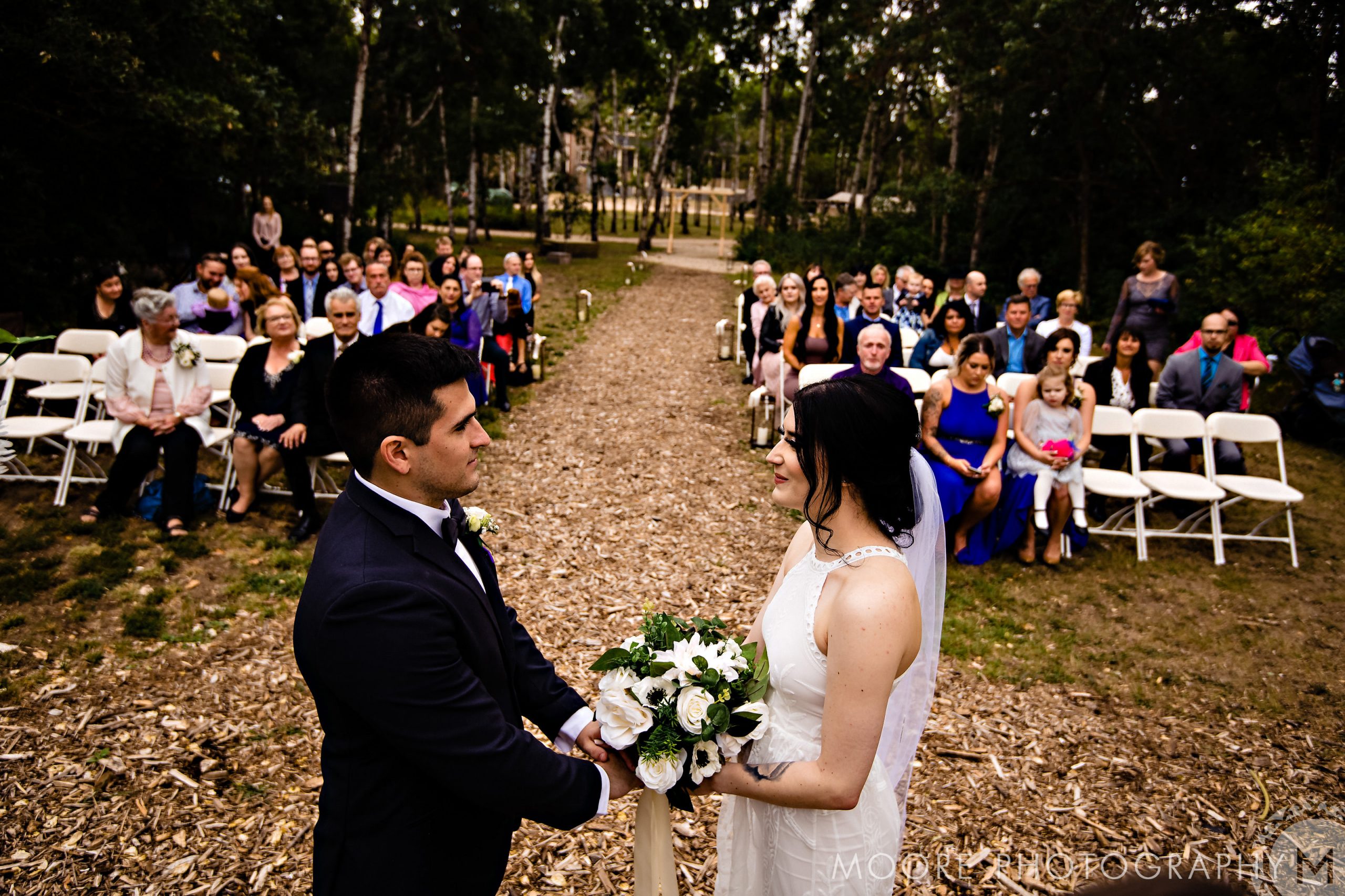 Bride and groom stand facing each other at a Winnipeg wedding venue with guests seated.