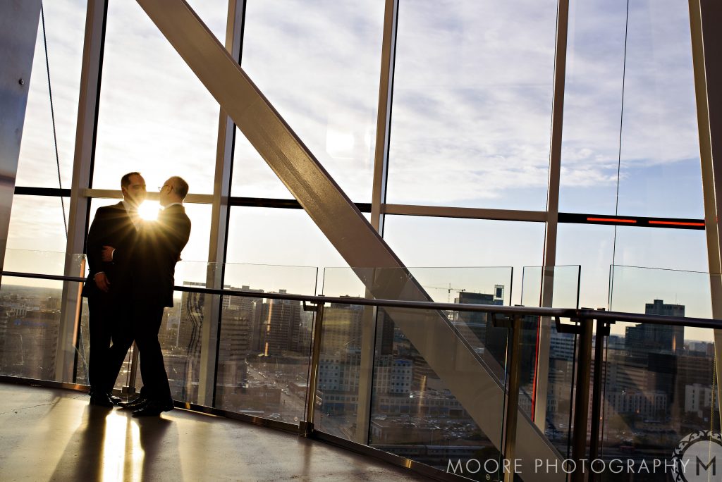 Two people in suits stand by large windows, with a cityscape and Winnipeg wedding venues.