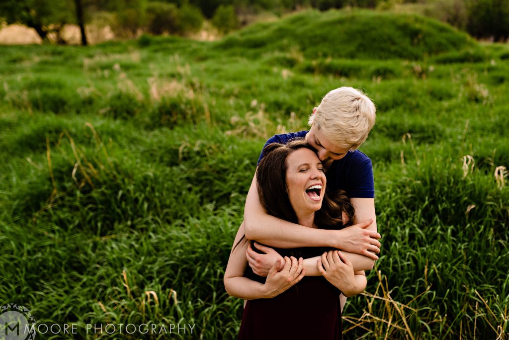 Lesbian posing, and laughing for an engagement photo in a Cinnabon forest