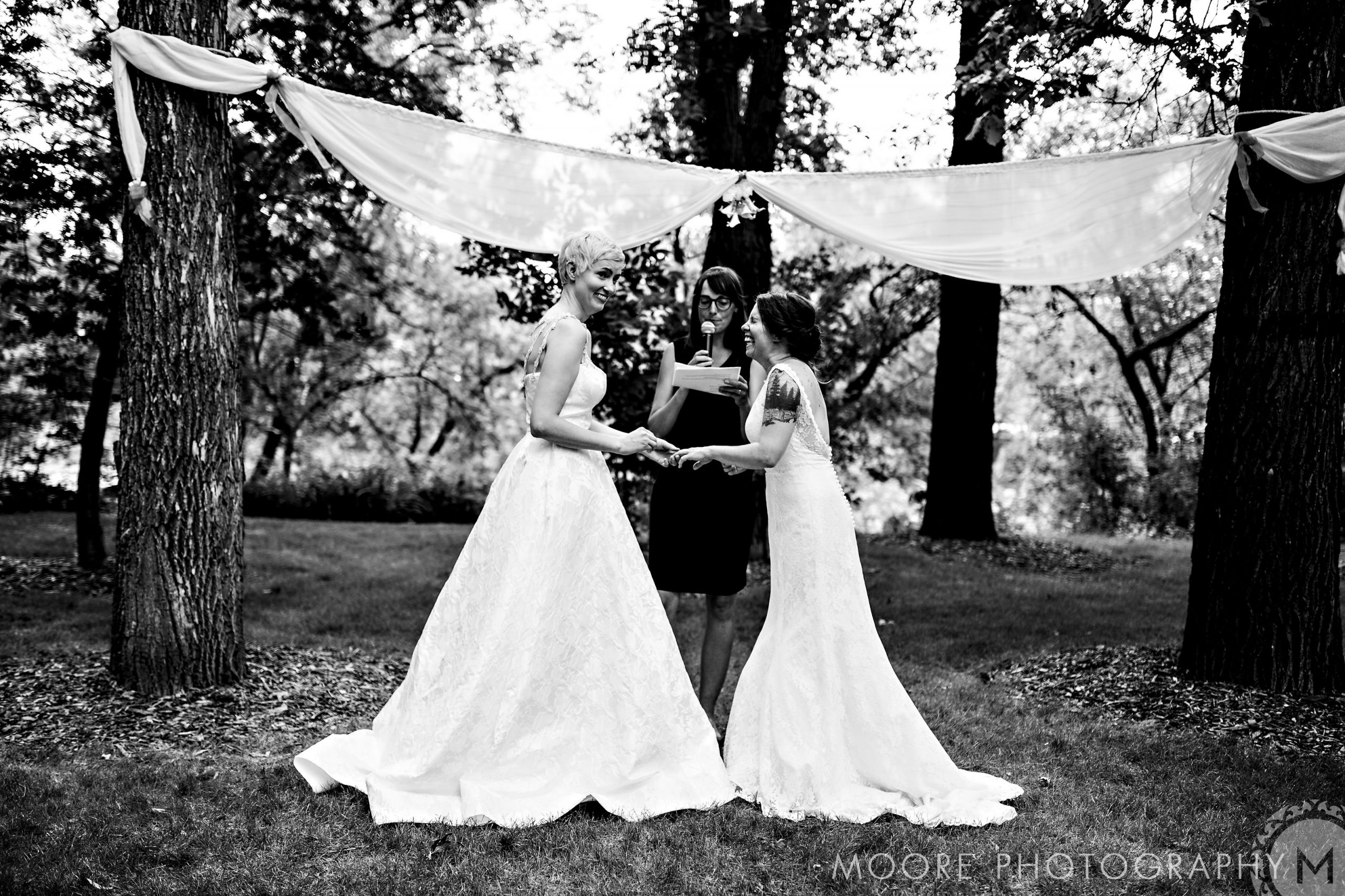 Two brides holding hands at a stunning Winnipeg wedding venue under a canopy.
