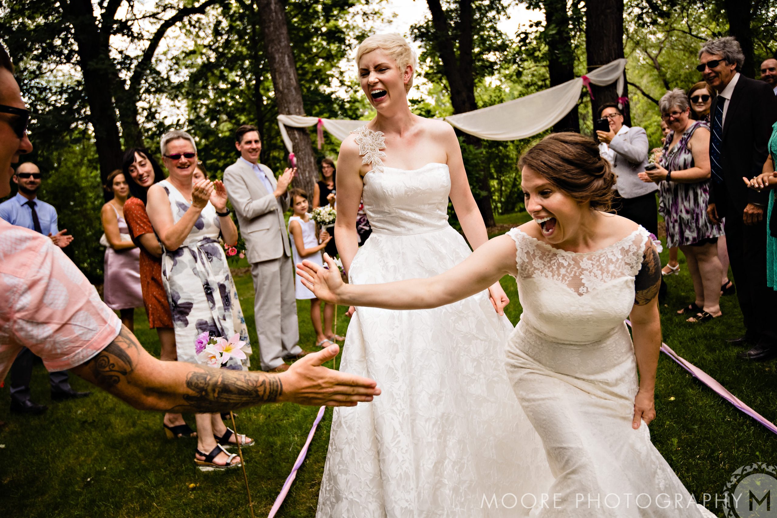 Two brides celebrating outdoors at beautiful Winnipeg wedding venues as guests cheer.