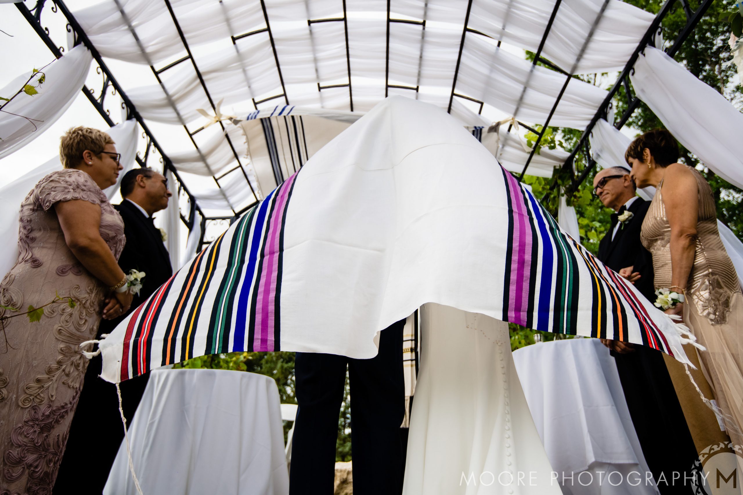 Lively Jewish wedding under chuppah with stripes; four attendees, two on each side.