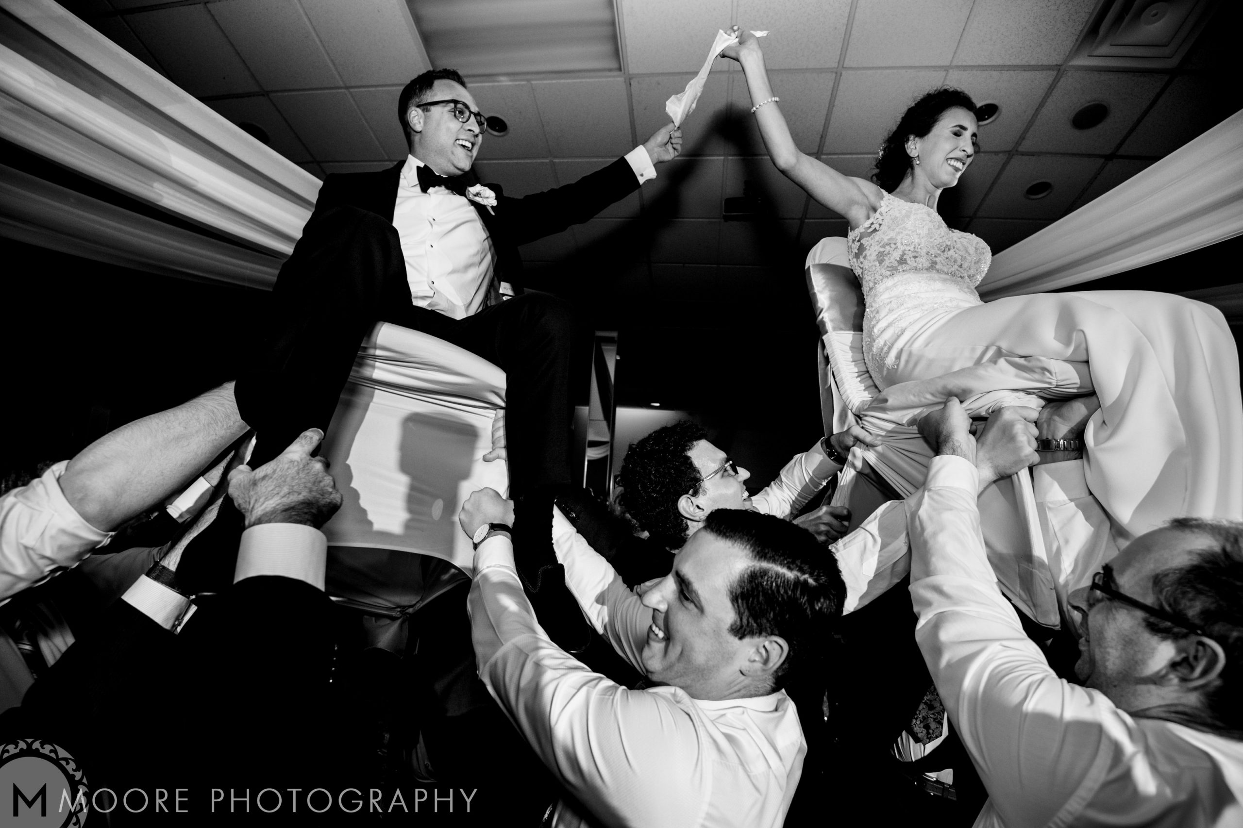 A couple lifted on chairs during a lively Jewish wedding celebration.