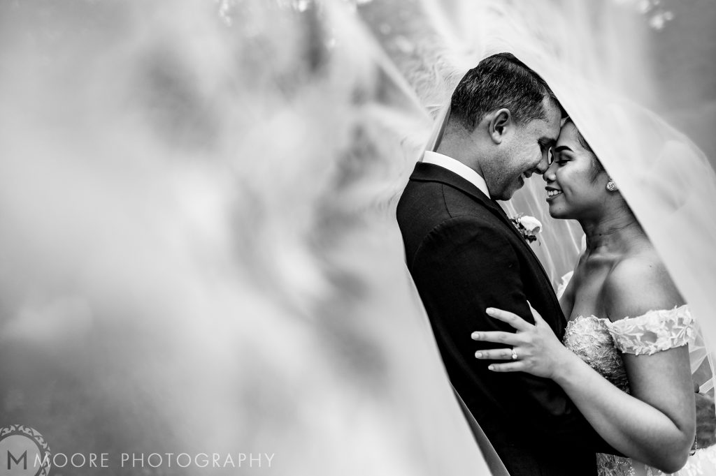 Bride and groom, embracing and smiling under the brides viel in Assiniboine Park