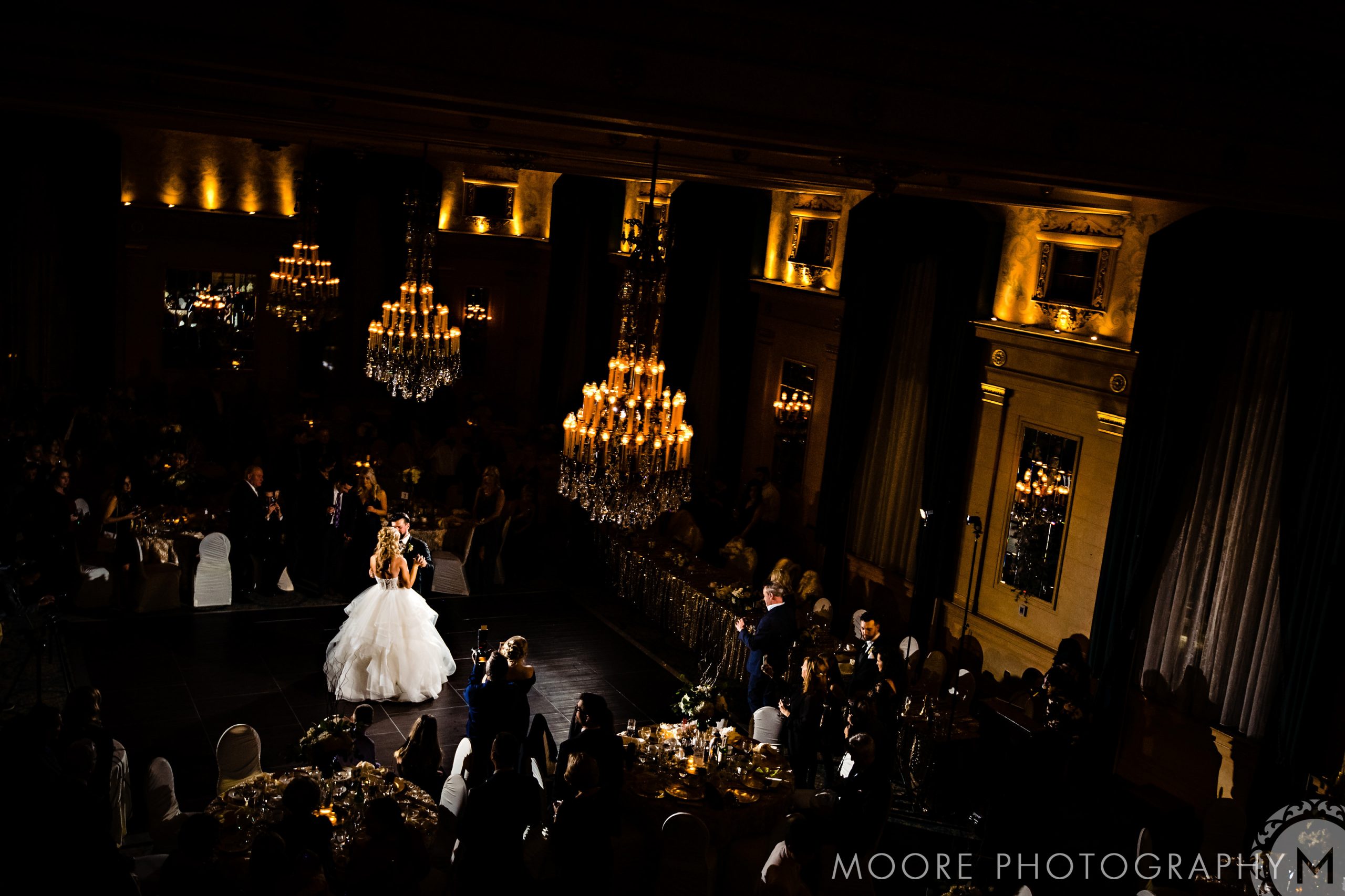 Bride and groom dance under chandeliers in a dimly lit Winnipeg wedding venue.
