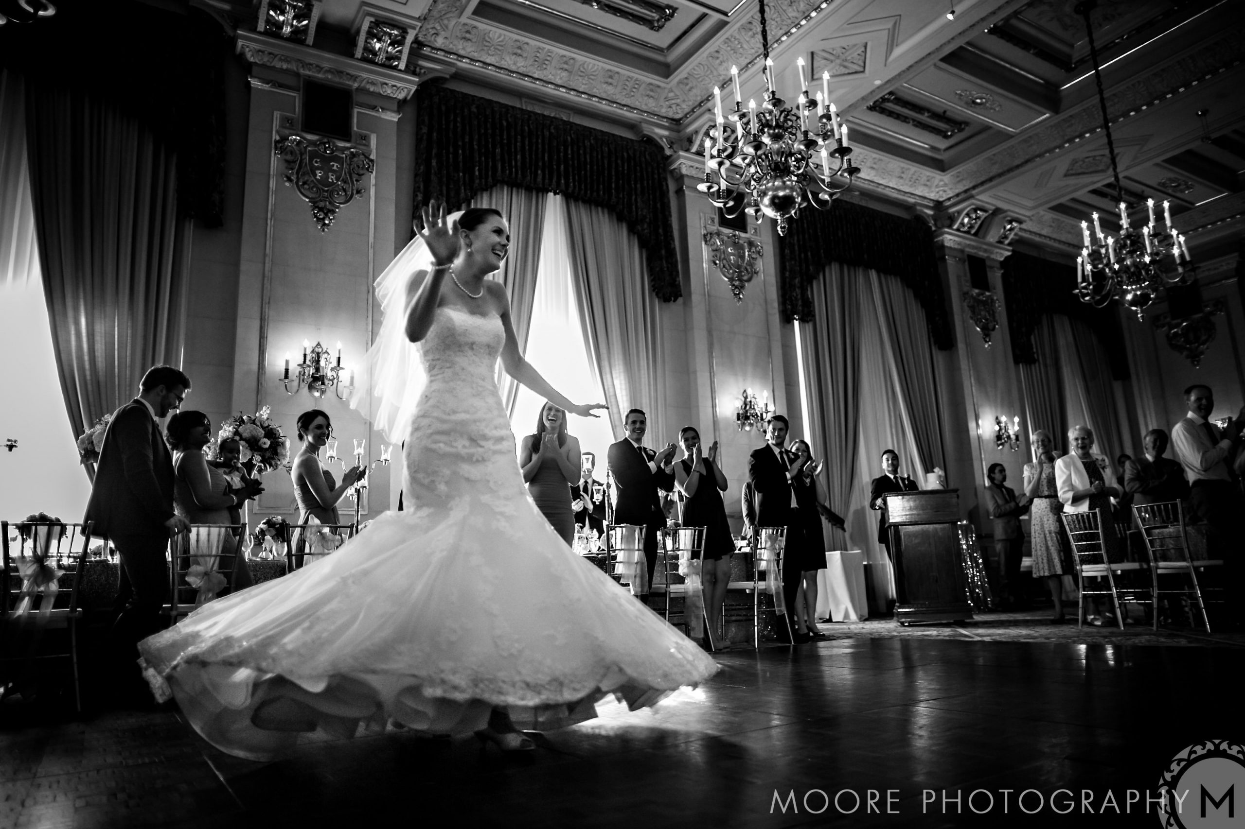 Bride joyfully dances in a Winnipeg wedding venue, surrounded by applauding guests.