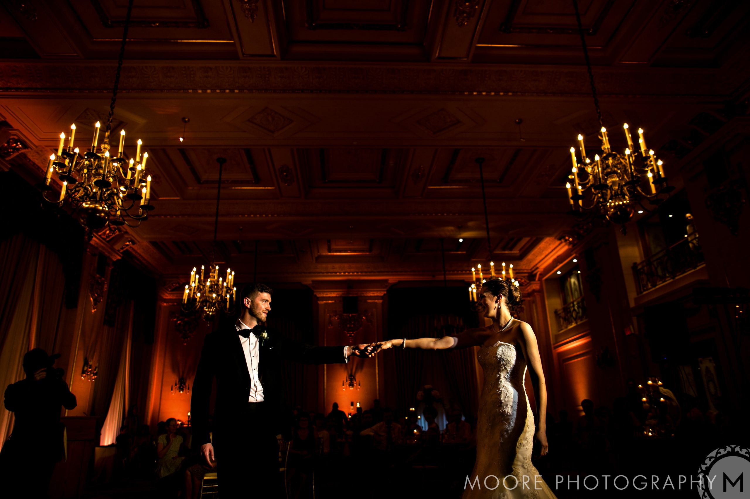 Couple elegantly dancing in a grand Winnipeg wedding venue with chandeliers and dim lighting.