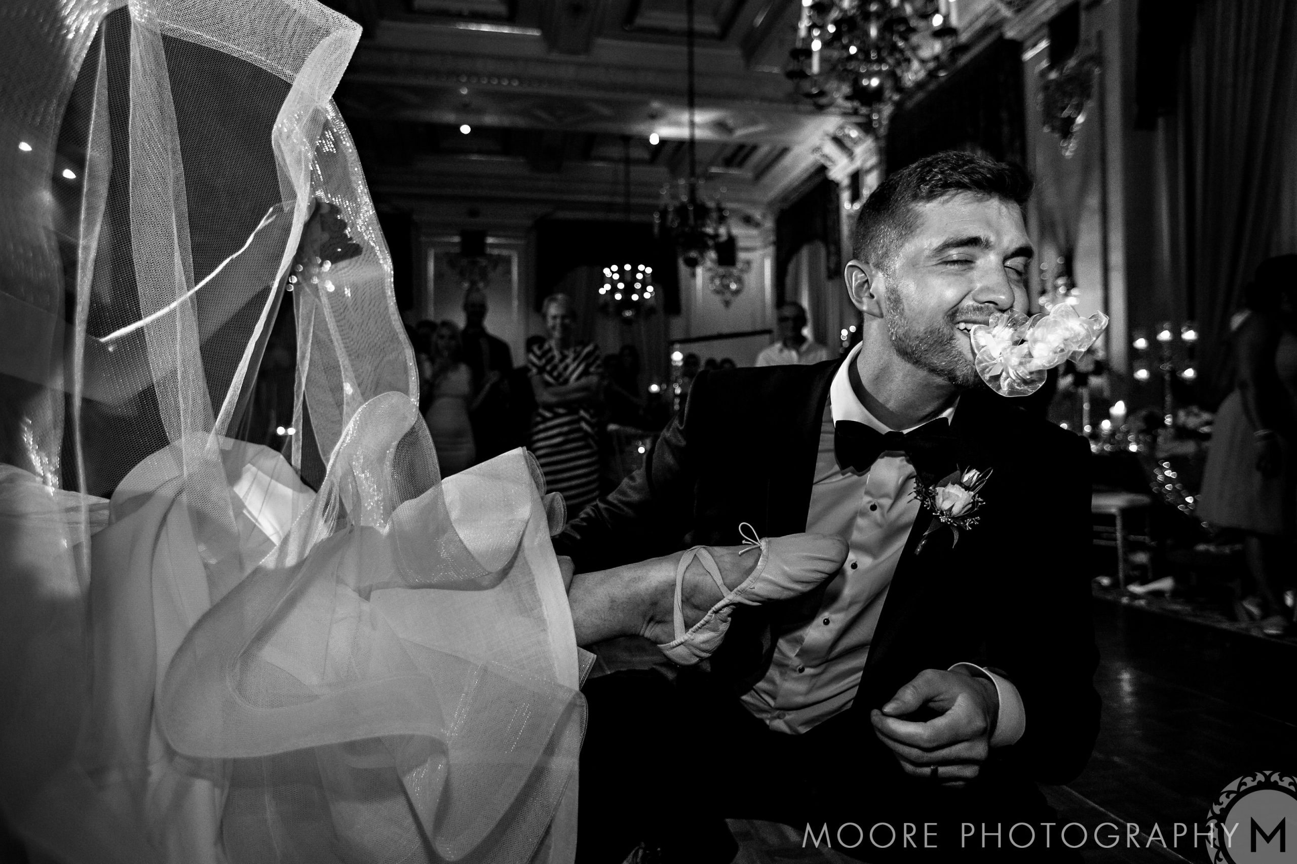 Groom laughing with a garter in his mouth at a Winnipeg wedding reception dance.