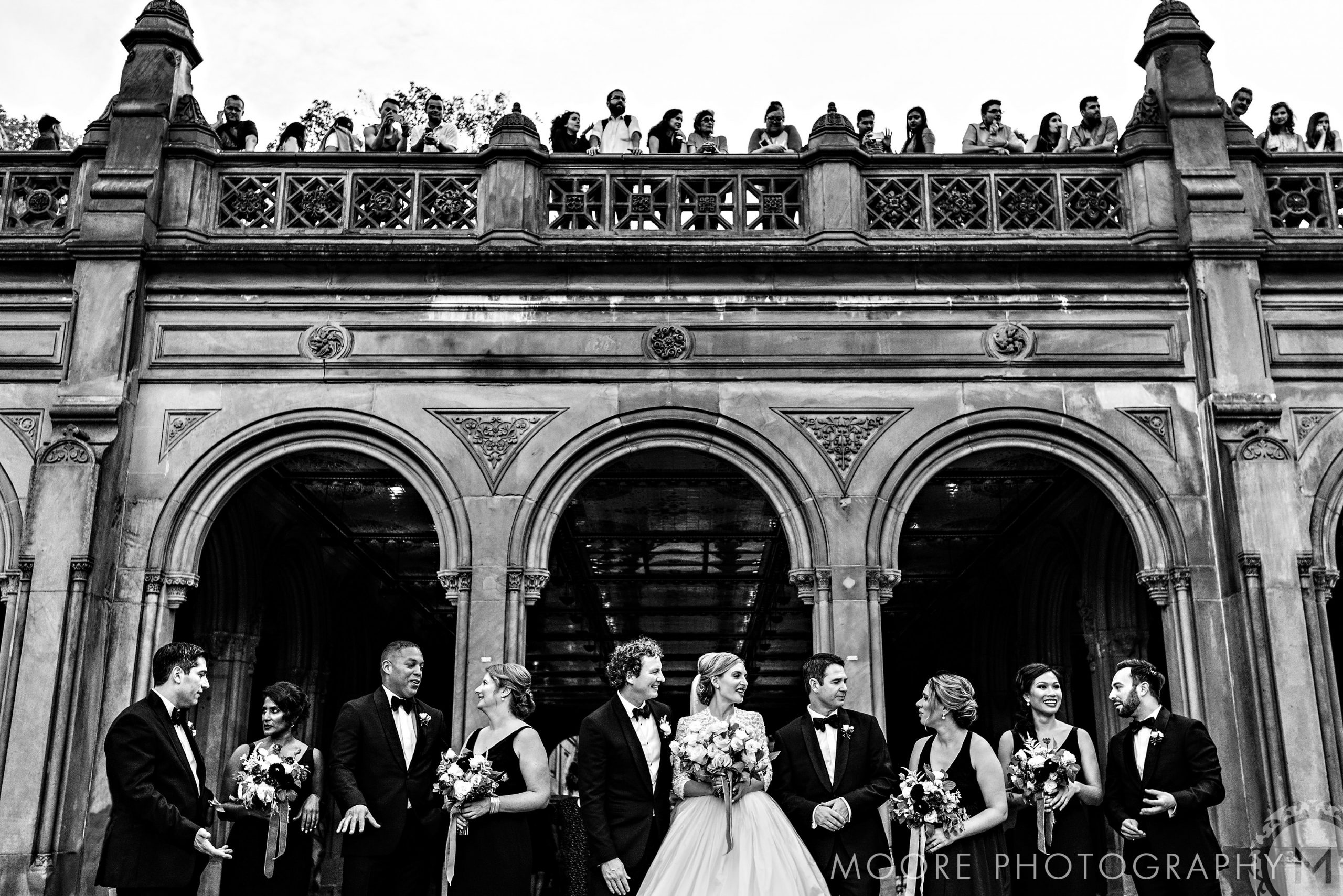 New York City destination wedding party posing; onlookers admire the ornate arches from above.