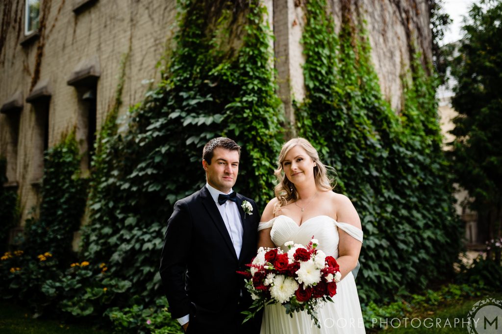A bride and groom posing for a photo in front of a vine and building in Winnipeg Manitoba