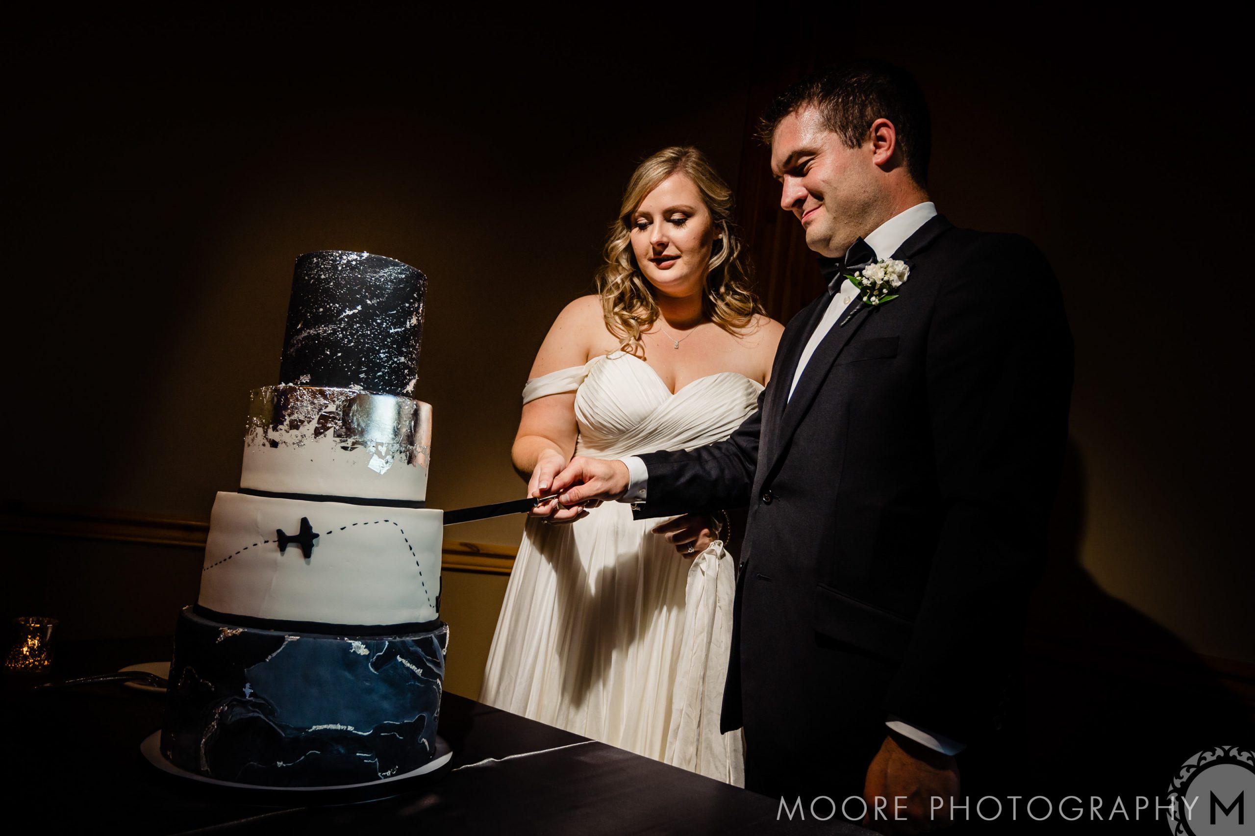 Couple at Winnipeg wedding venues cuts a travel-themed black and white cake.