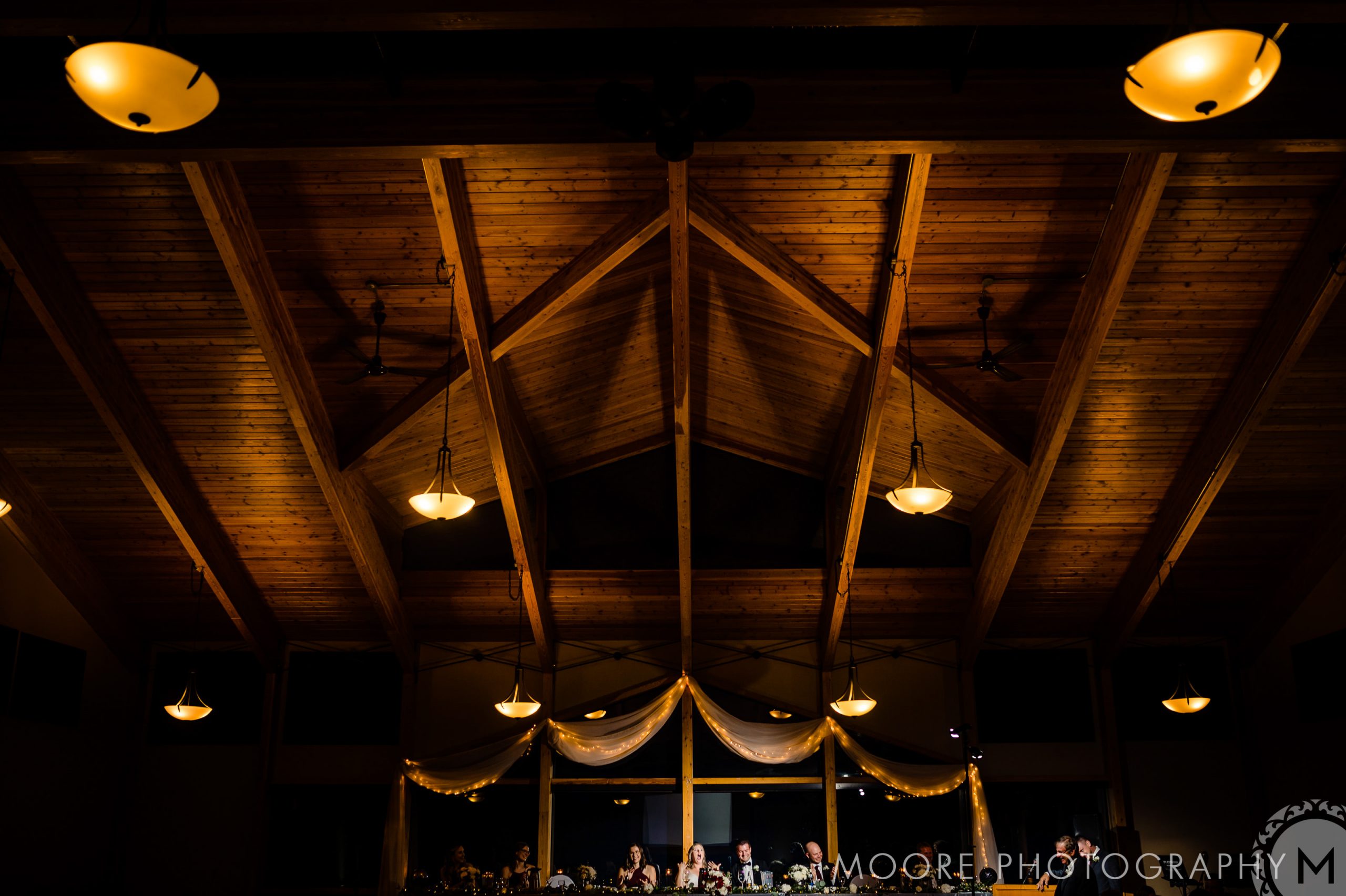 Dimly lit wooden ceiling with hanging lamps, draped fabric over a large window—perfect for Winnipeg wedding venues.