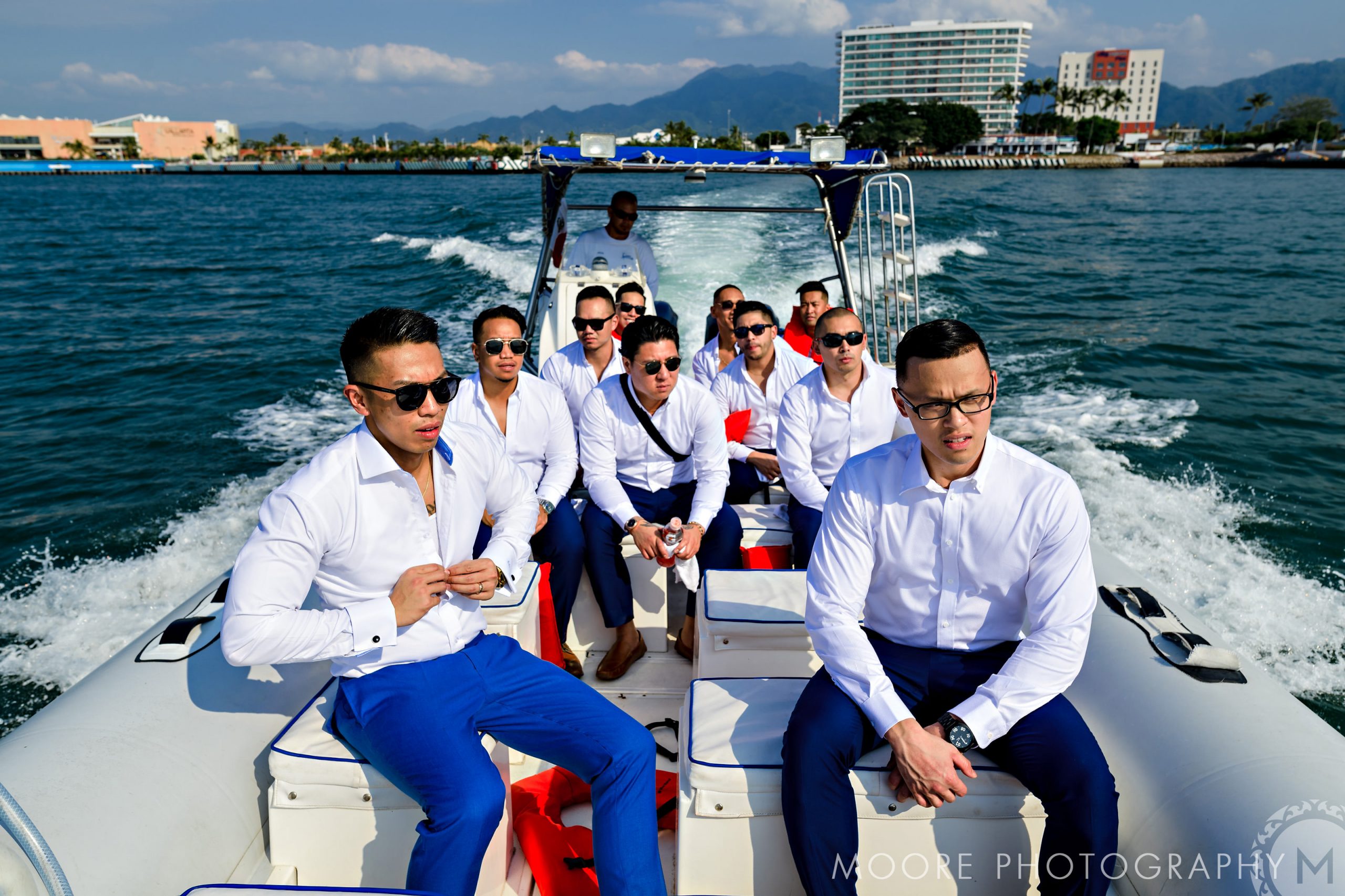 Group of men in white shirts on a speedboat with Puerto Vallarta as the stunning backdrop.
