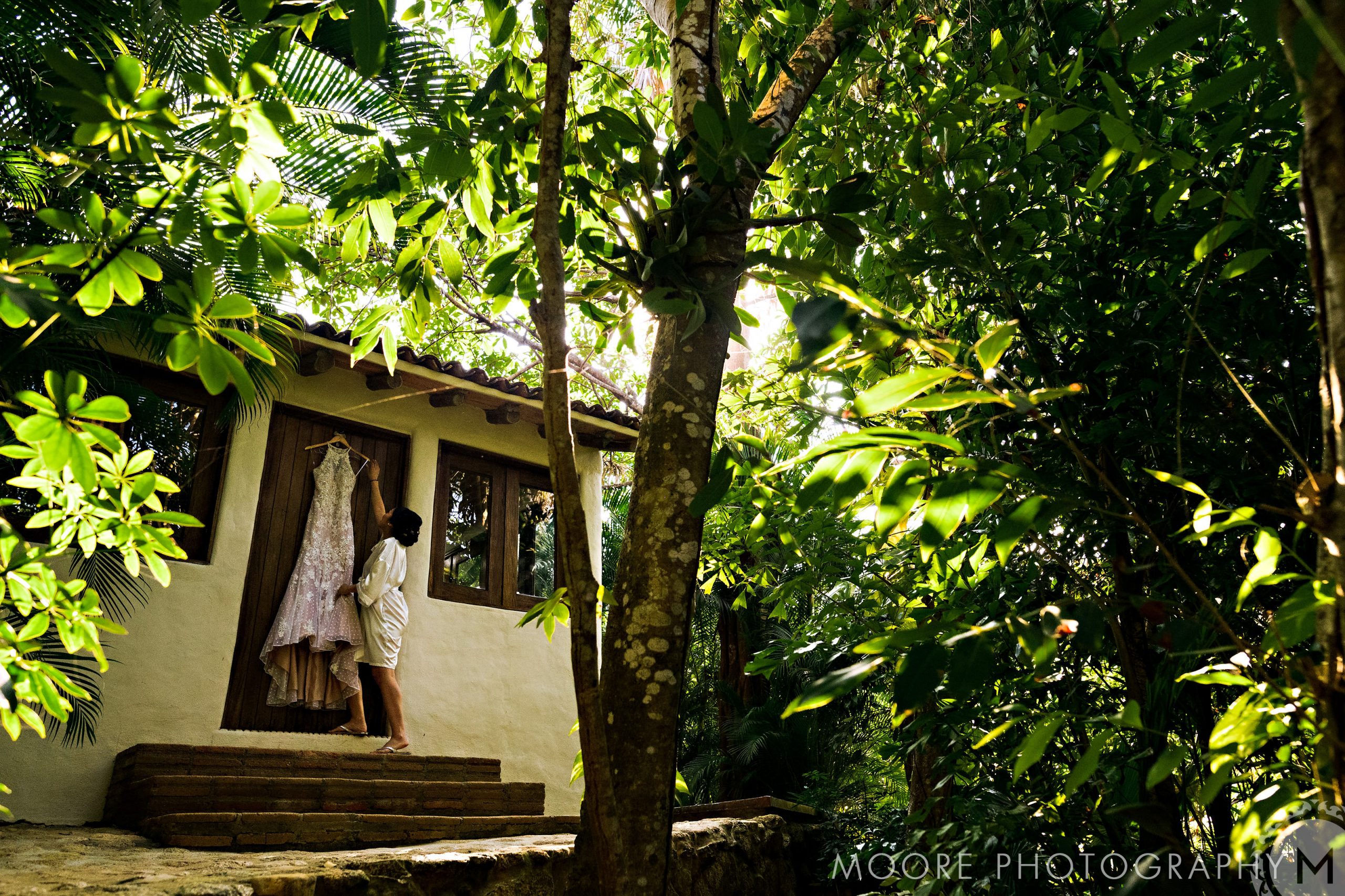 A person admires a dress by a house amidst Puerto Vallarta's lush wedding greenery.