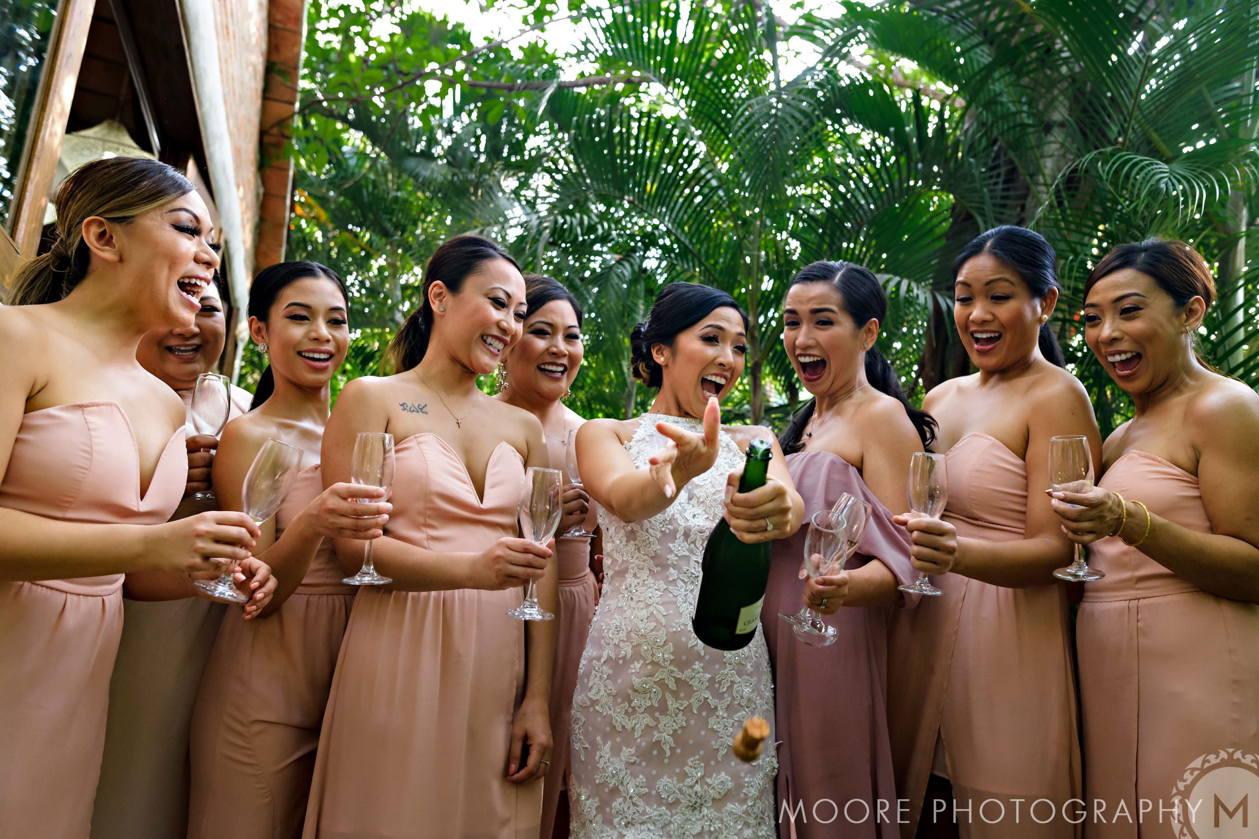Bride popping champagne with bridesmaids in pink at a lush Puerto Vallarta destination wedding.