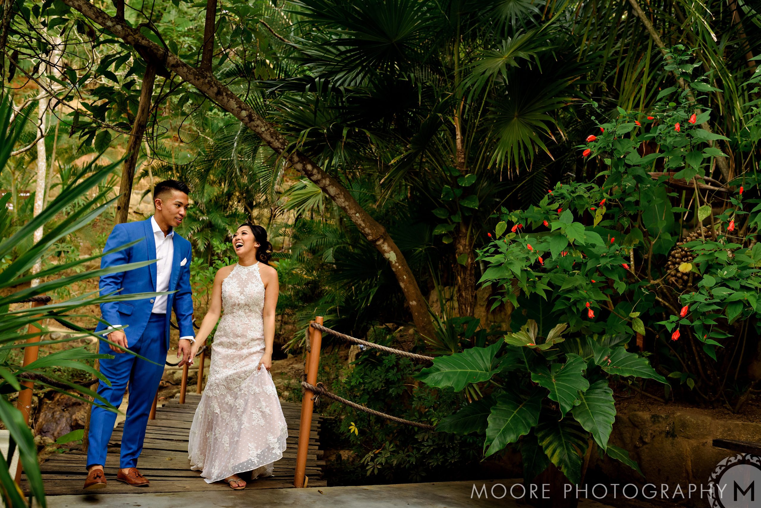 Couple in wedding attire laughing on a lush tropical path in Puerto Vallarta.