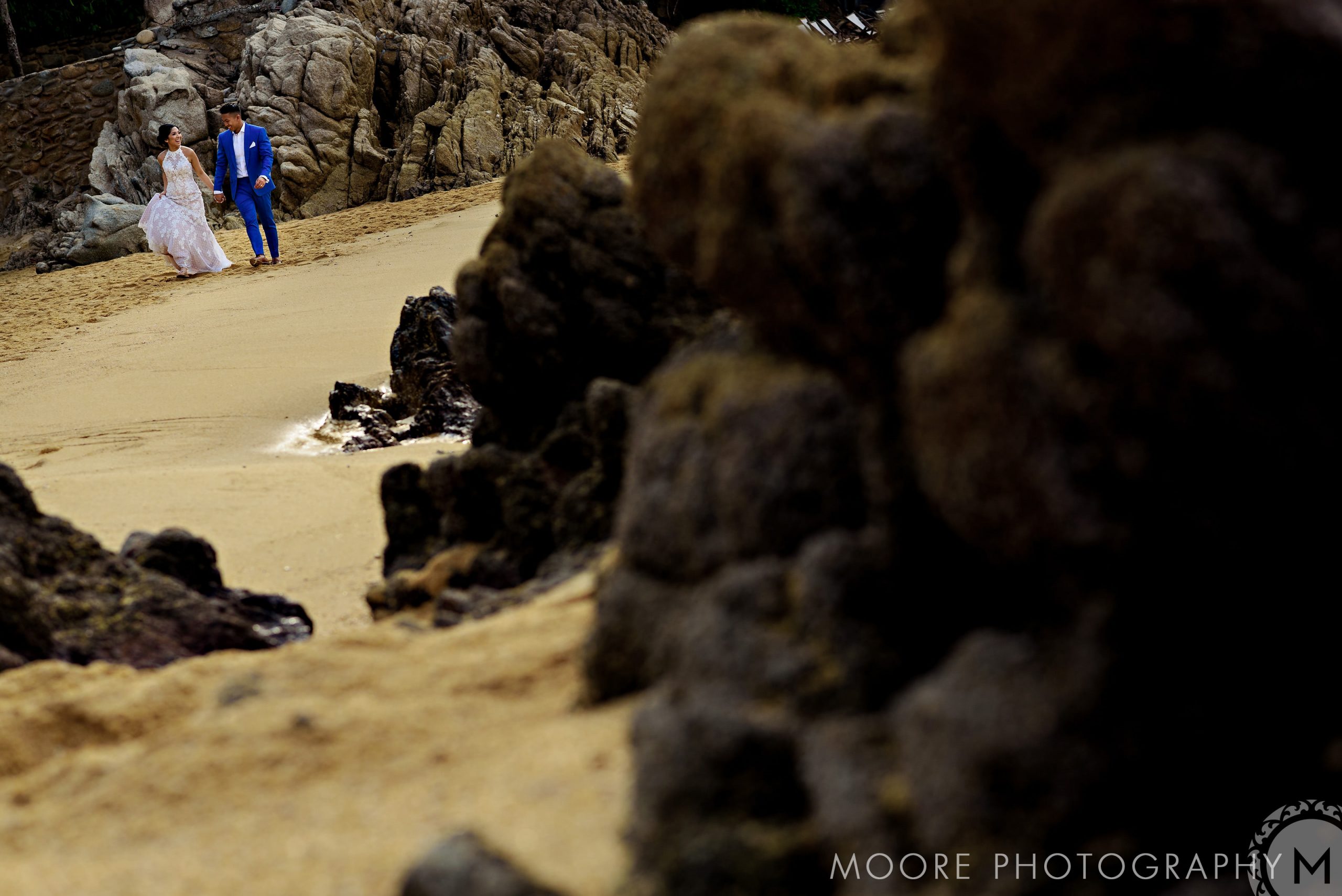 Bride and groom on a rocky beach, captured low-angle for a Puerto Vallarta wedding.