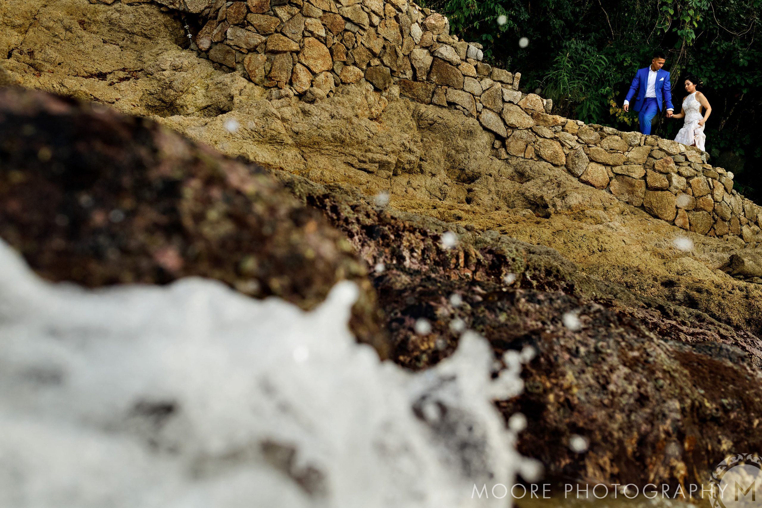 Couple in wedding attire on rocky path by the ocean, Puerto Vallarta's charm surrounding them.