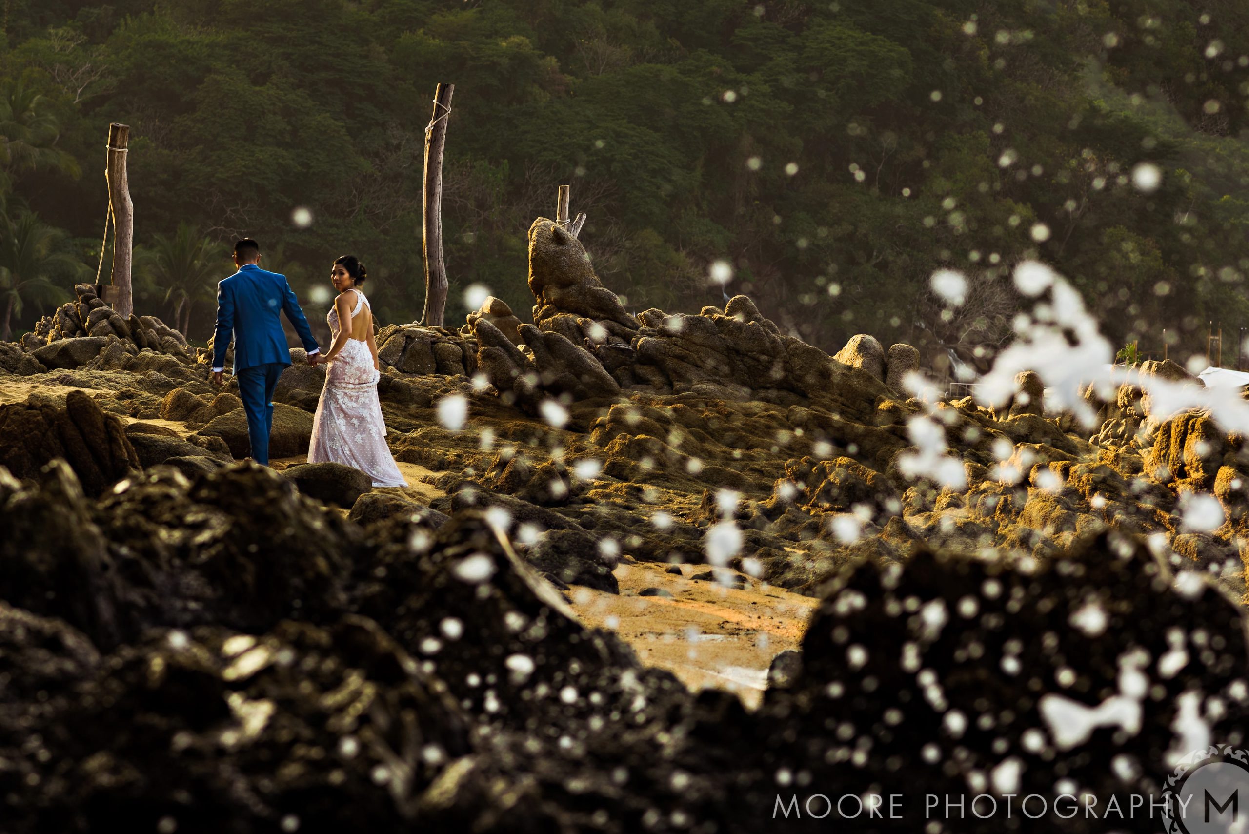 Couple walking on rocky shore in Puerto Vallarta, crashing waves in the foreground.